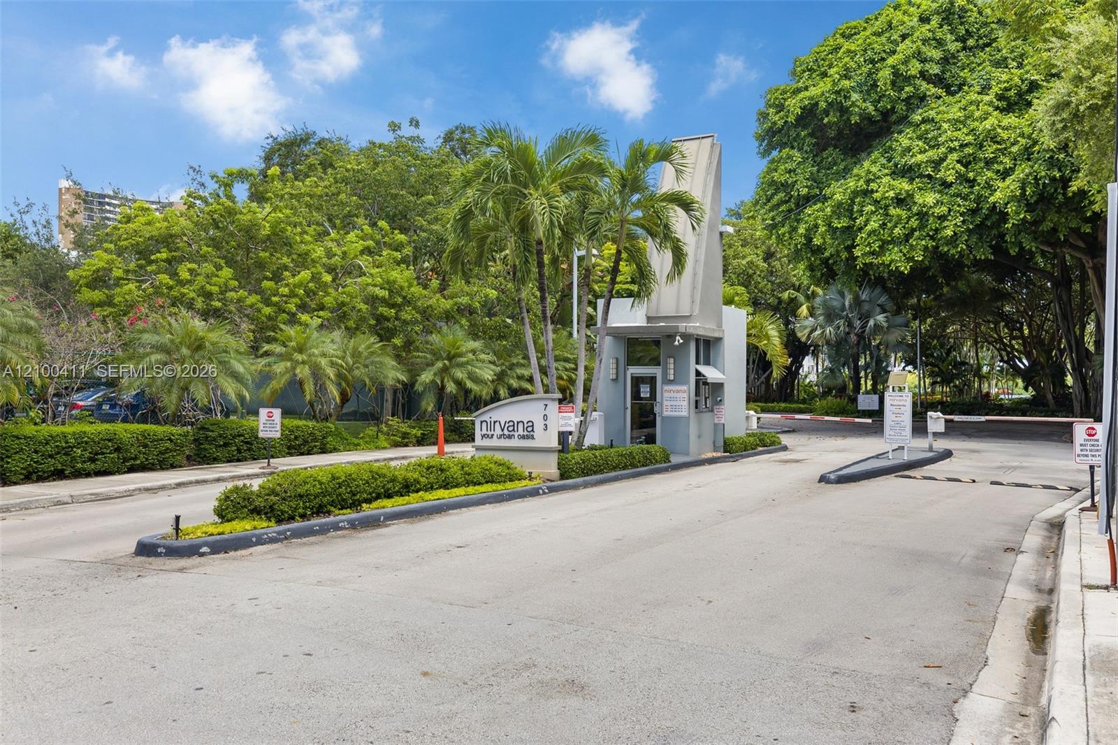 Gated entry featuring a controlled-access security booth, paved roadway, and mature landscaping