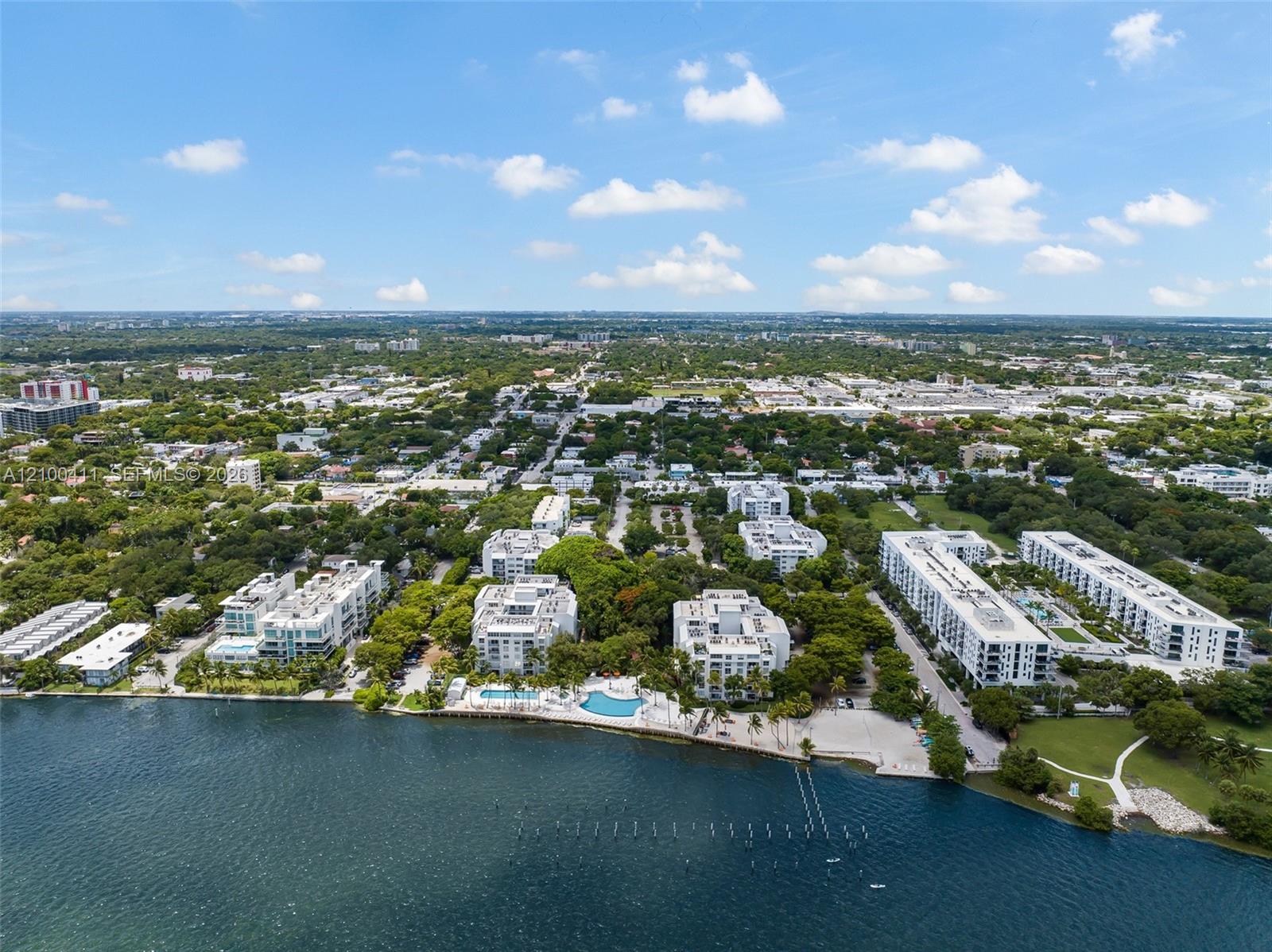 Waterfront setting featuring multiple swimming pools, paved walking paths, expansive green spaces, and mature tree canopy