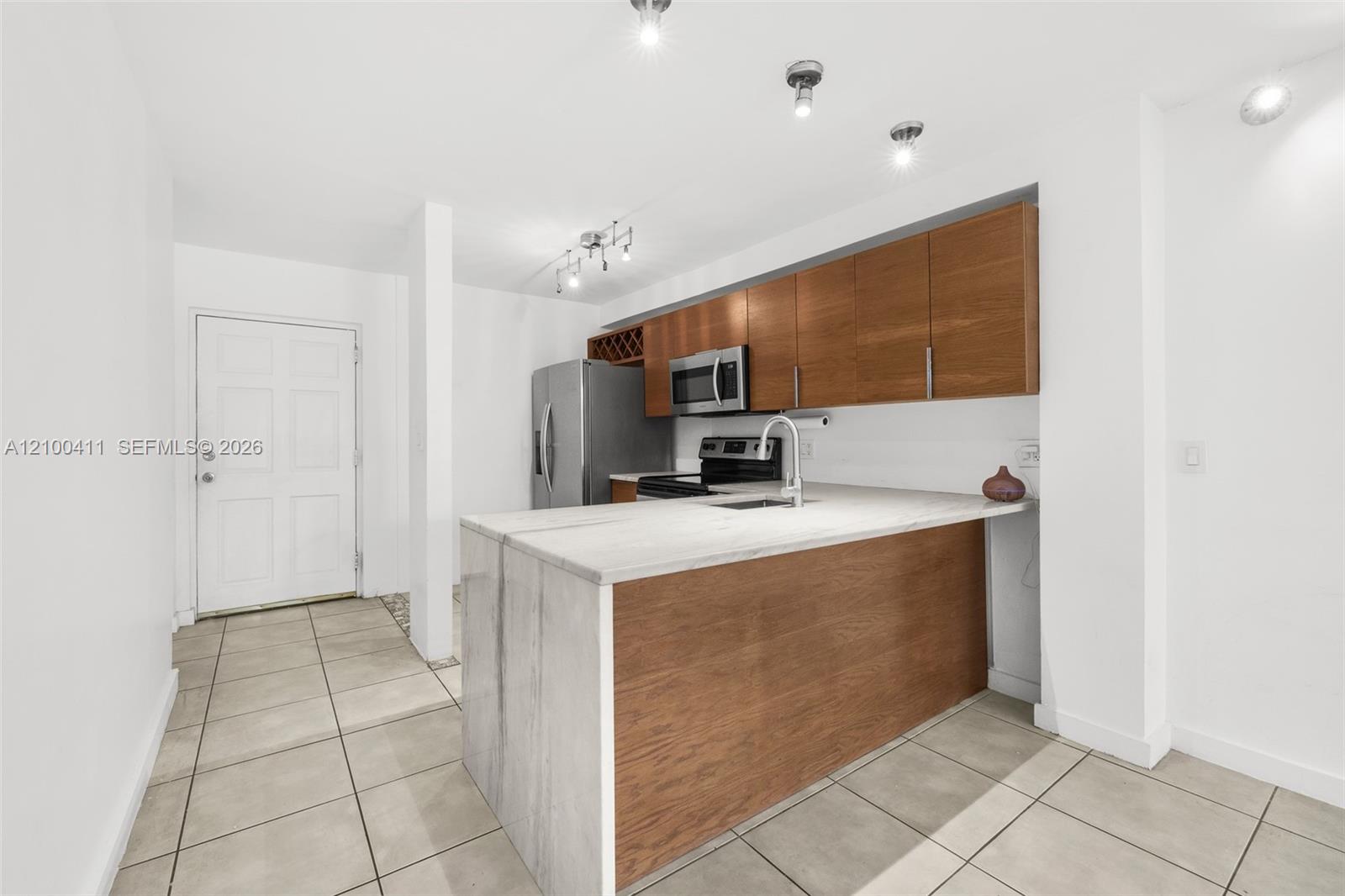 Kitchen featuring flat-panel wood-finish cabinetry, stainless steel appliances, stone-surface peninsula, and tile flooring