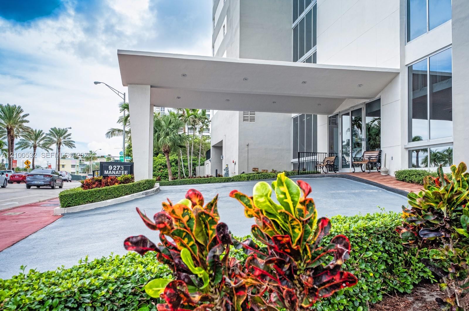 Covered porte-cochre entry featuring recessed lighting, glass-paneled entrance doors, multi-story building facade, and manicured landscaping