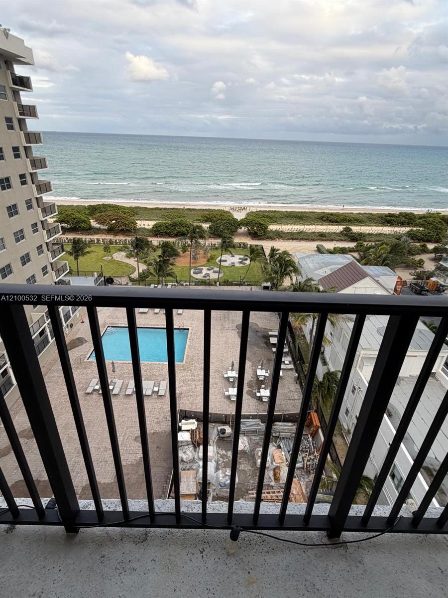 Balcony featuring a black metal railing, overlooking a swimming pool, landscaped grounds, and the ocean shoreline