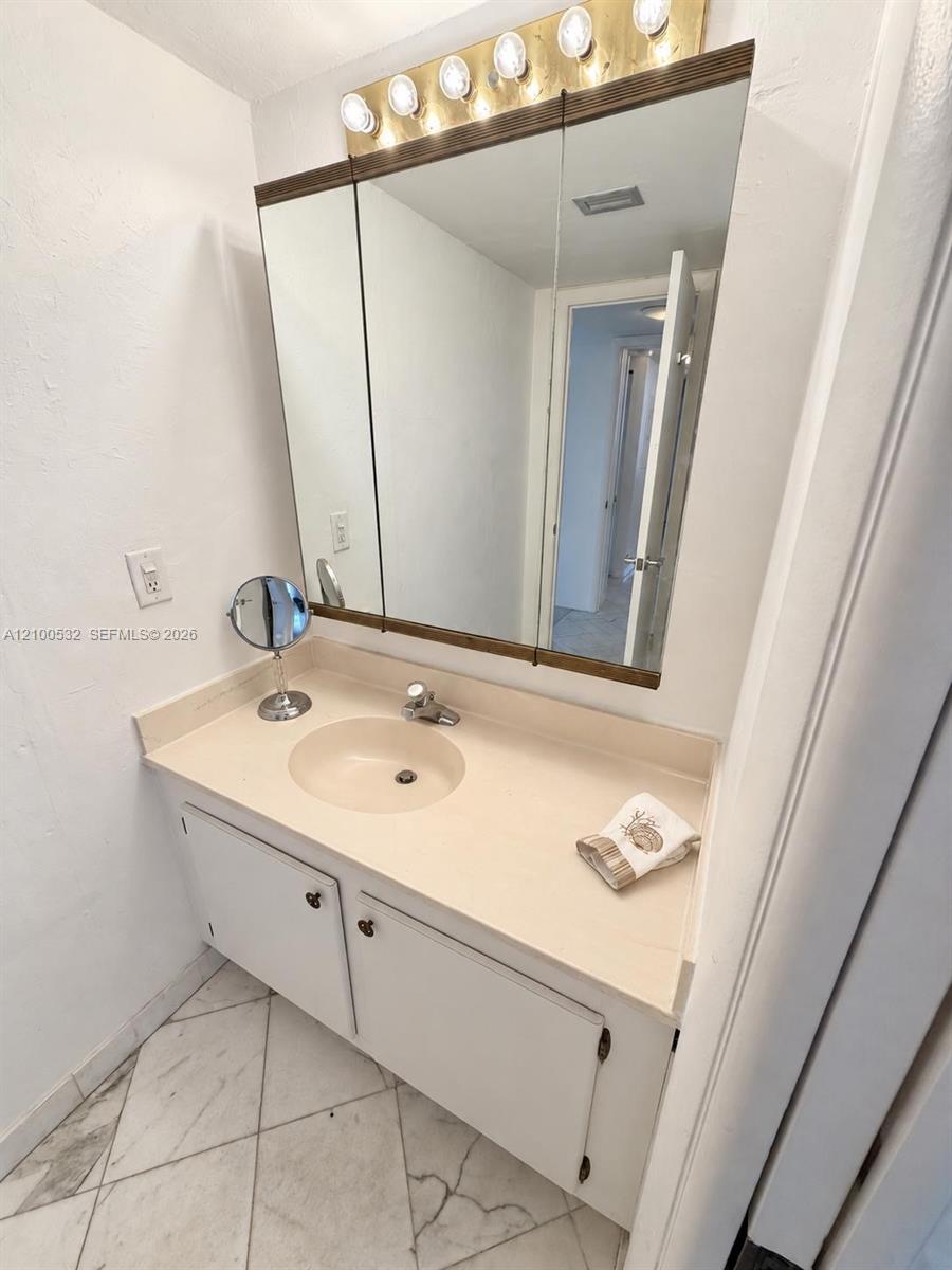 Vanity featuring a solid surface countertop with an integrated sink, three-panel medicine cabinet, five-bulb light fixture, and stone-finish tile flooring