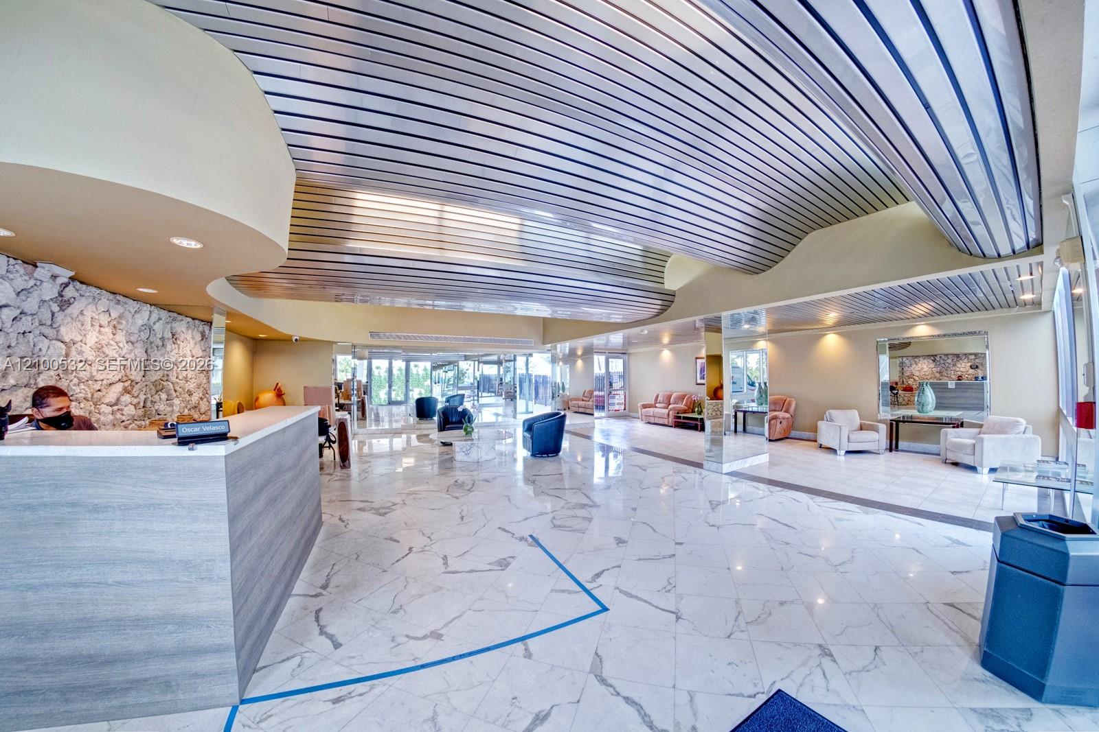 Spacious interior featuring a metallic corrugated ceiling, polished stone flooring, a large reception desk with wood-finish paneling, and an accent wall composed of natural stone