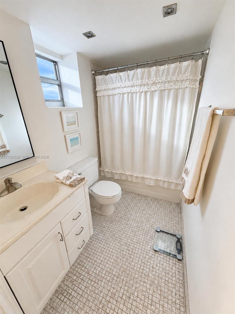 Bathroom featuring a white vanity cabinet, integrated sink with a metal faucet, mosaic tile flooring, and a tub-shower combination with recessed ceiling lighting