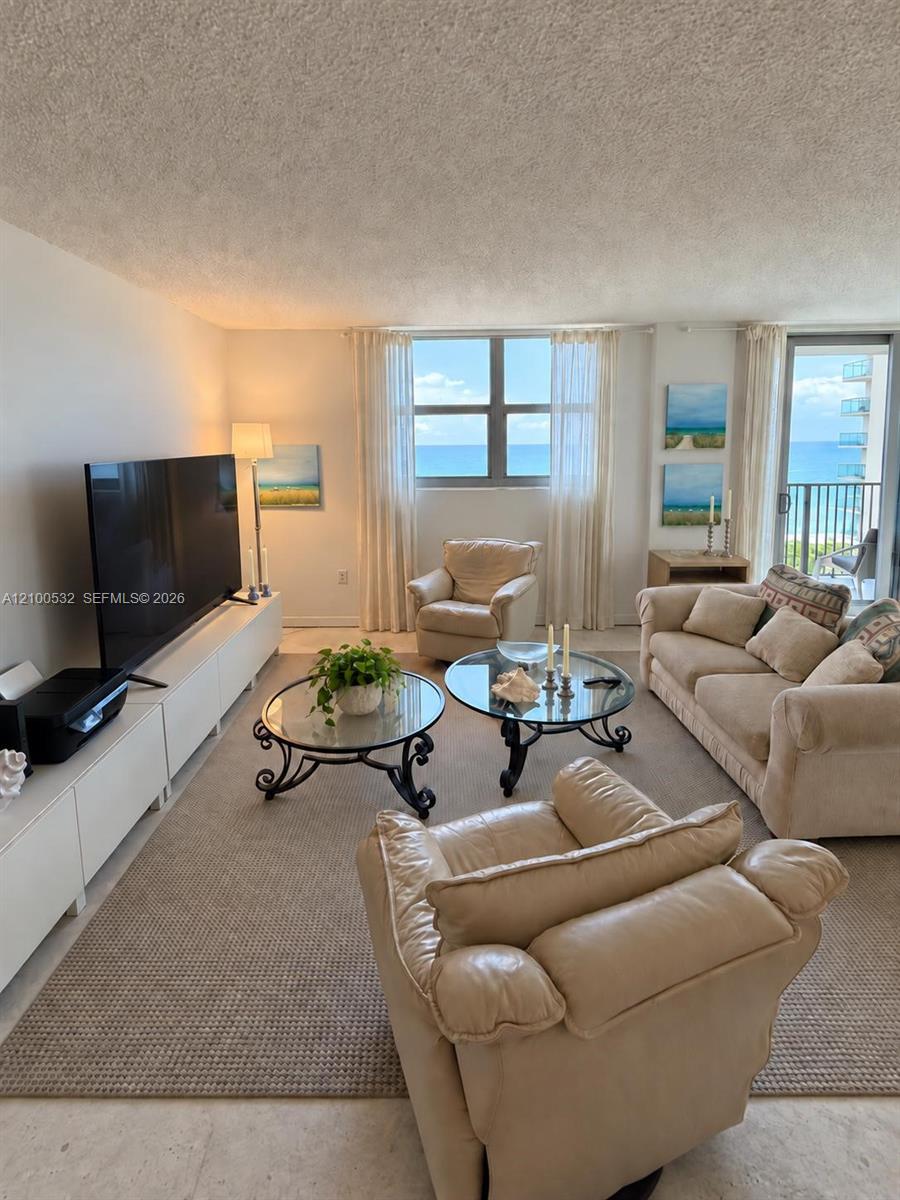 Living area featuring large windows, integrated storage cabinetry, neutral wall-to-wall carpeting, and a glass sliding door providing access to a balcony with ocean exposure