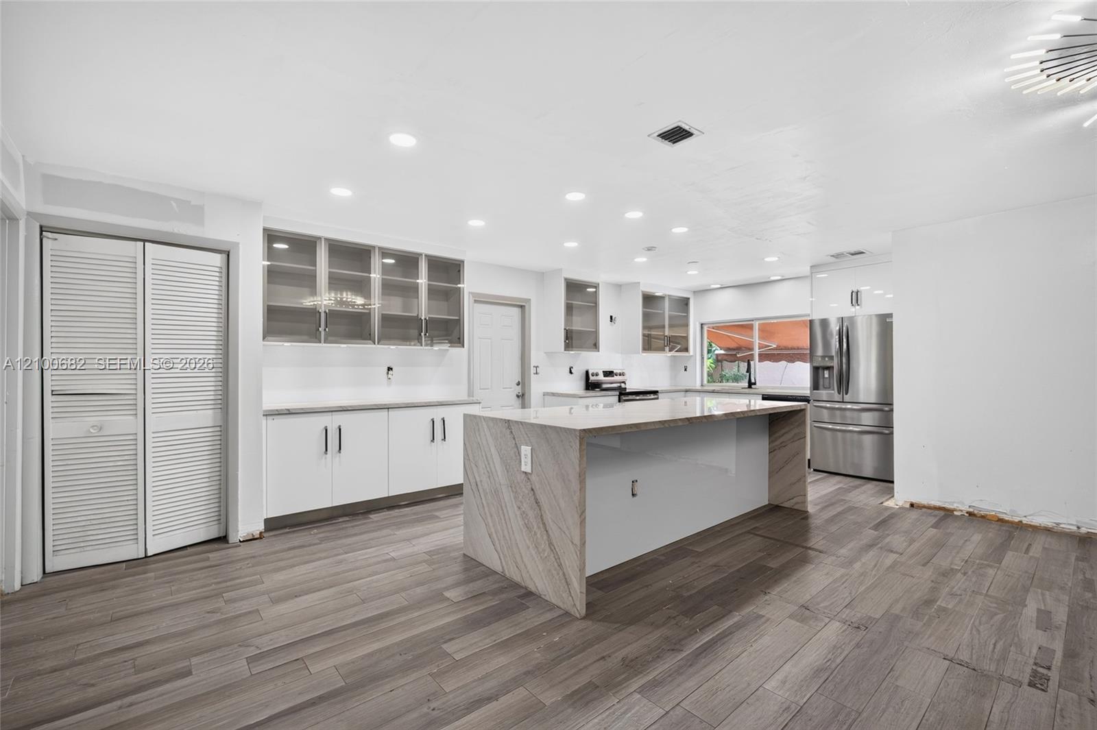 Kitchen featuring vinyl plank wood flooring, quartz-surfaced countertops and taj majal island with waterfall edge, white cabinetry, glass-front upper cabinets, and recessed ceiling lighting