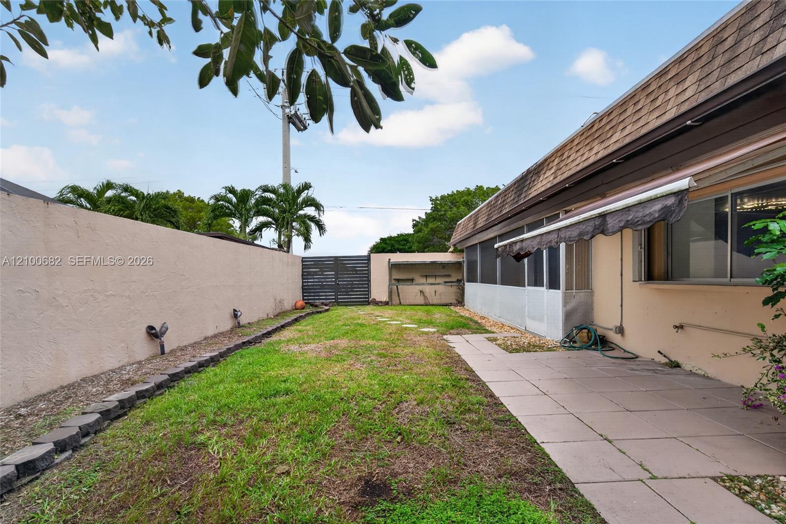 Back yard featuring a concrete paver patio, screened-in enclosed patio, perimeter privacy wall, and newer horizontal slat gate*