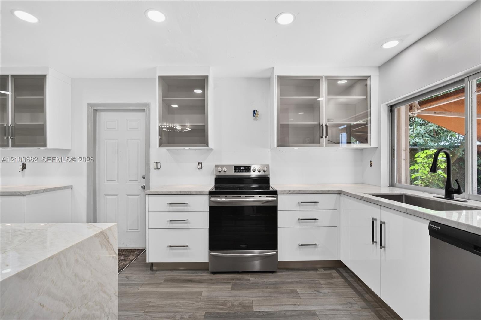 Kitchen featuring white cabinetry with glass-front uppers, solid surface countertops, stainless steel appliances, recessed lighting, and vinyl wood-finish flooring