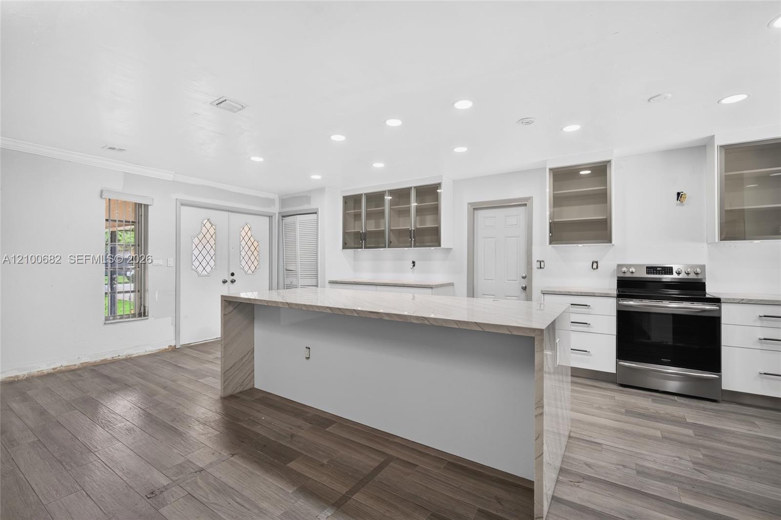 Kitchen featuring a waterfall-edge stone island, vinyl wood-finish flooring, white cabinetry, recessed lighting, and stainless steel range