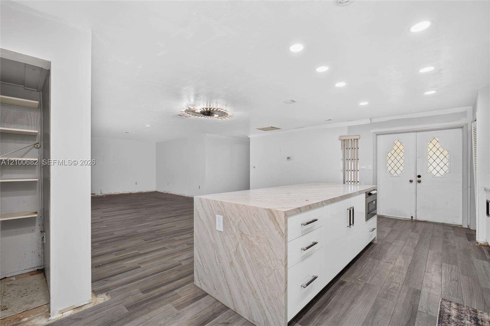 Expansive room featuring vinyl wood-finish flooring, a large kitchen island with stone-finish countertop & microwave, recessed lighting, double-door entryway, deep pantry on the side *