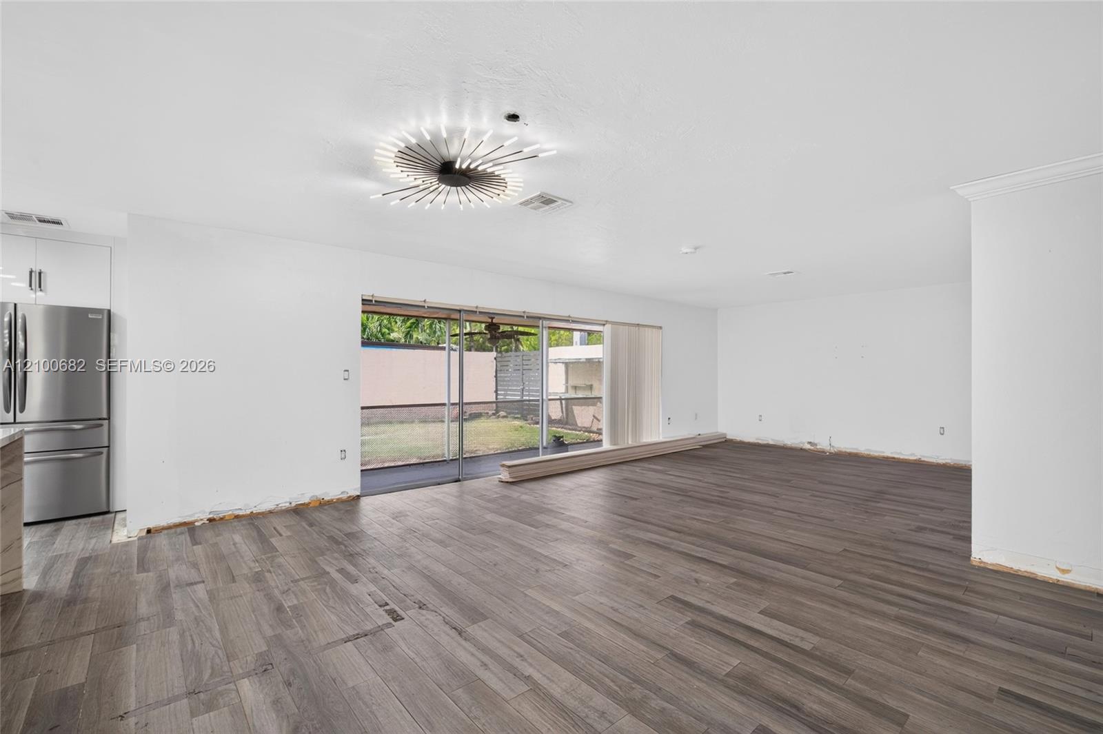 Open-concept interior featuring vinyl wood-finish flooring, a modern starburst-style ceiling light fixture, and large sliding glass doors to the covered patio*