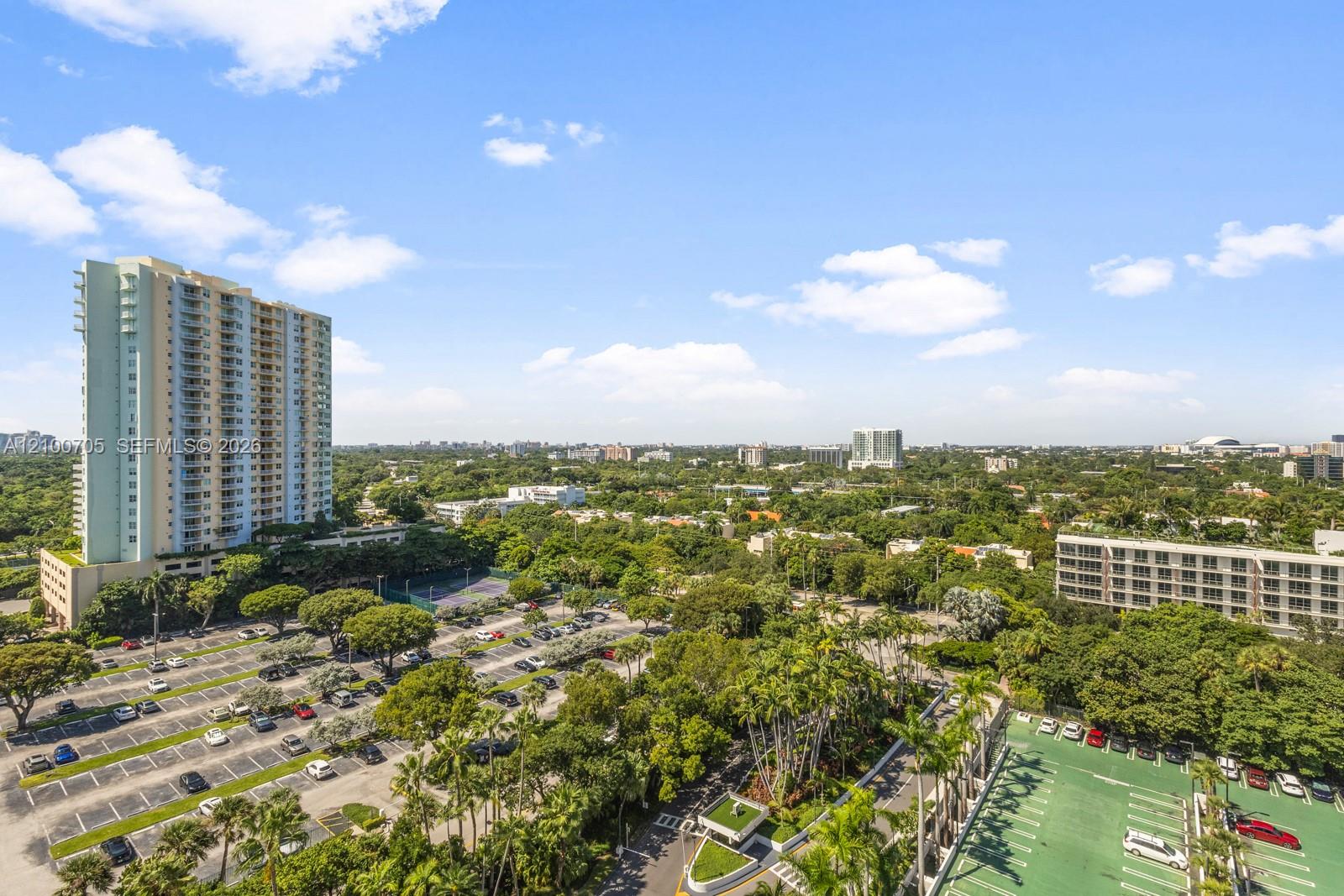 Elevated perspective featuring sprawling canopy coverage, mature palm trees, paved parking infrastructure, and mid-rise residential architecture