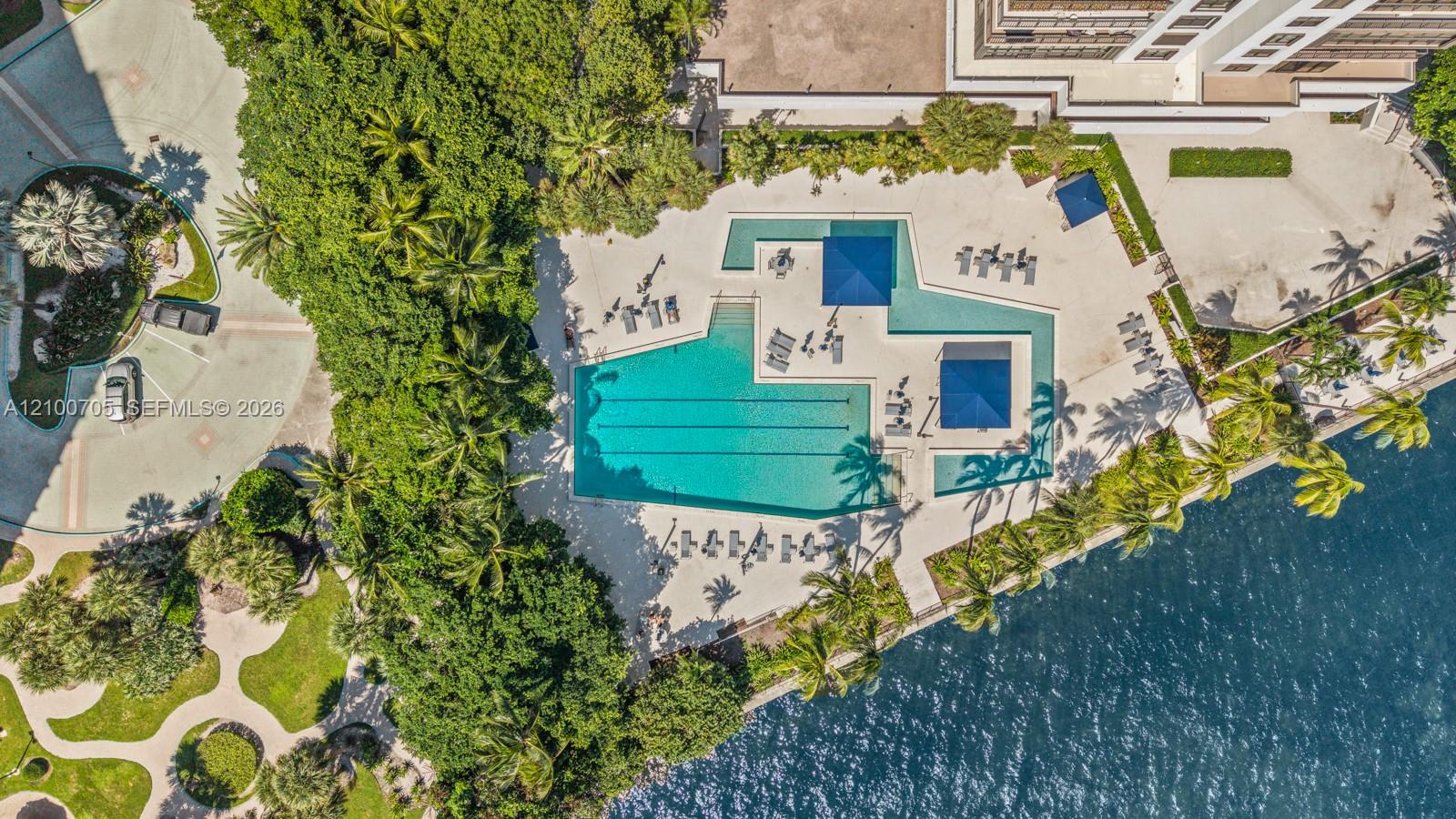 Aerial perspective of a multi-level swimming pool with lap lanes and integrated shade structures, situated within landscaped grounds and located along the waters edge