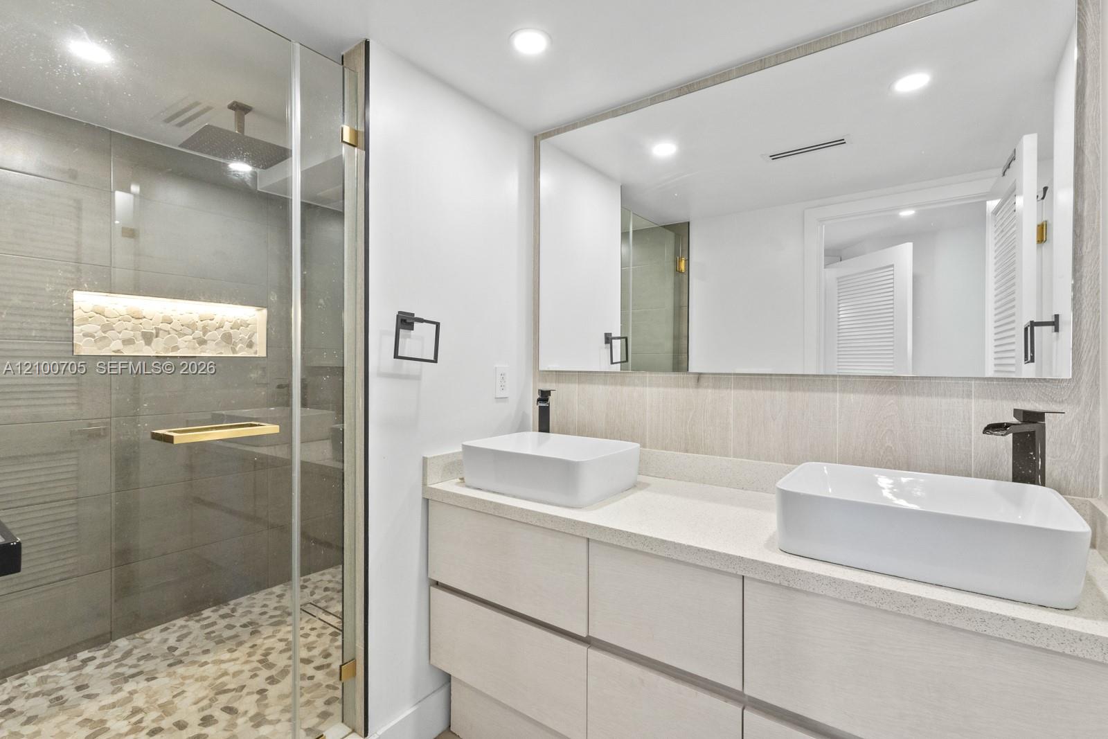 Double vanity featuring rectangular vessel sinks, stone-finish countertops, matte black fixtures, and a glass-enclosed shower with pebble tile flooring and a built-in stone niche