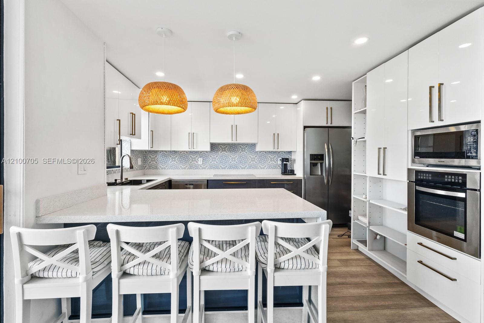 Kitchen featuring gloss-finish cabinetry, quartz countertops, patterned tile backsplash, stainless steel built-in double oven, and wood-finish flooring