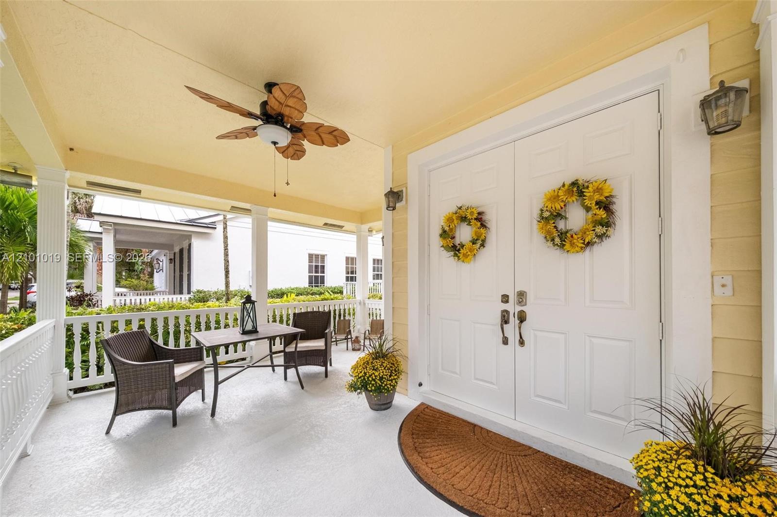 Covered front porch featuring a ceiling fan with leaf-style blades, painted white columns, a white balustrade railing, and double entry doors Covered front porch featuring a ceiling fan with leaf-style blades, painted white columns, a white balustrade railing, and double entry doors