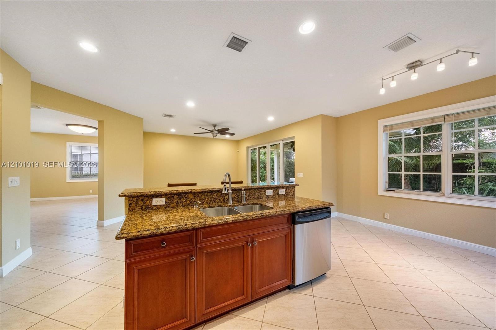 Kitchen island featuring stone countertops, integrated double-basin stainless steel sink, custom wood cabinetry, stainless steel dishwasher, and recessed lighting