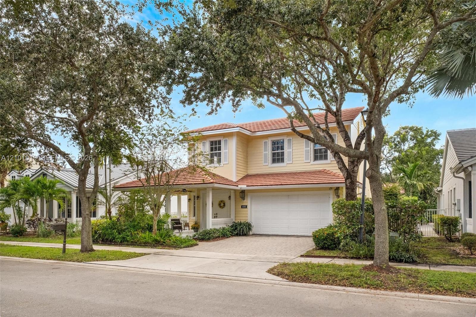 Two-story residence featuring light-colored siding, a tiled roof, a multi-car garage, and a covered front entry porch with a paved driveway Two-story residence featuring light-colored siding, a tiled roof, a multi-car garage, and a covered front entry porch with a paved driveway