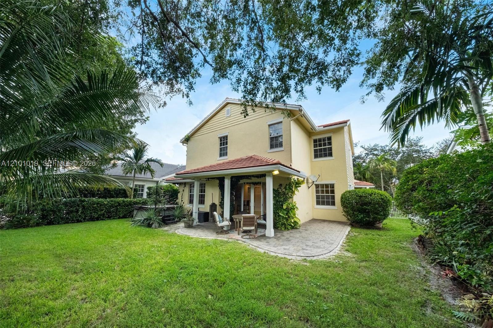 Stucco exterior featuring a covered patio with concrete pavers, a tile roof, mature landscaping, and an expansive lawn