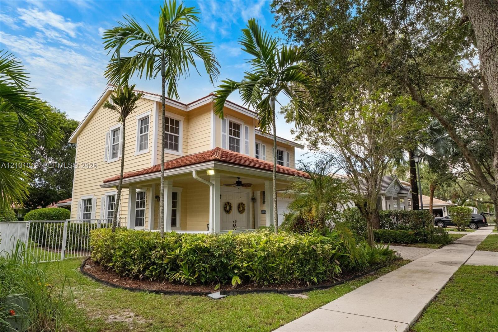 Two-story exterior featuring light yellow horizontal siding, a tiled roof, a covered front porch, and manicured landscaping Two-story exterior featuring light yellow horizontal siding, a tiled roof, a covered front porch, and manicured landscaping
