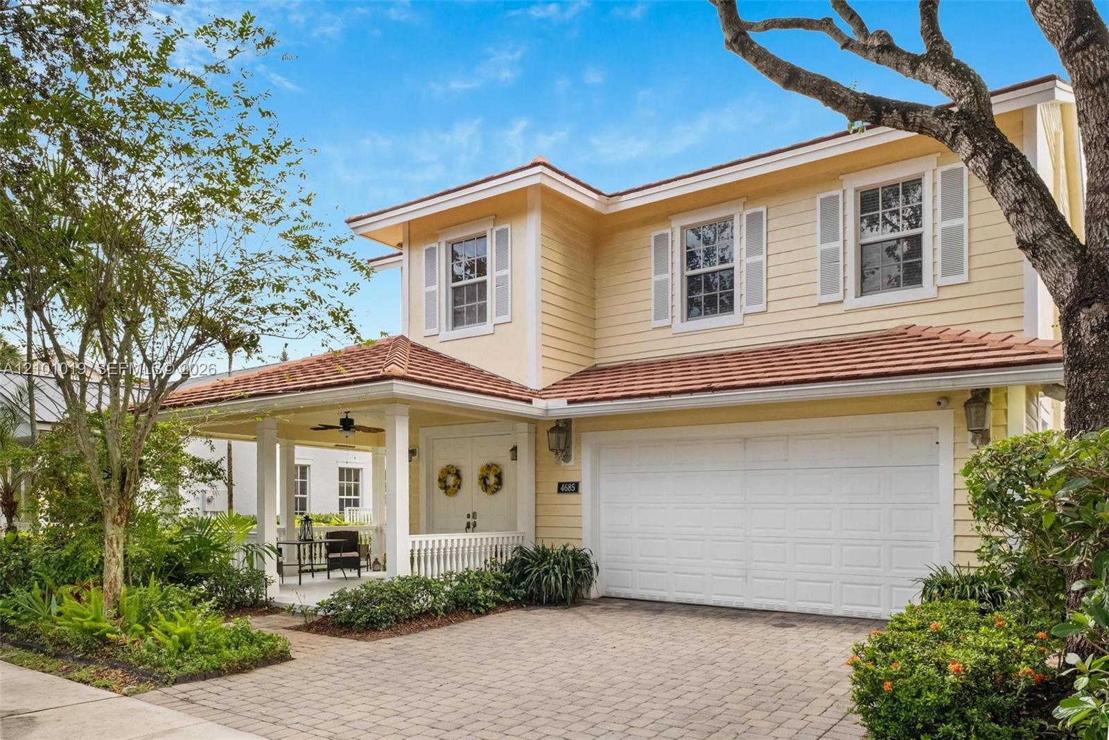 Two-story exterior featuring light-toned lap siding, a tile roof, a covered front porch with white railing, and a paved stone driveway Two-story exterior featuring light-toned lap siding, a tile roof, a covered front porch with white railing, and a paved stone driveway