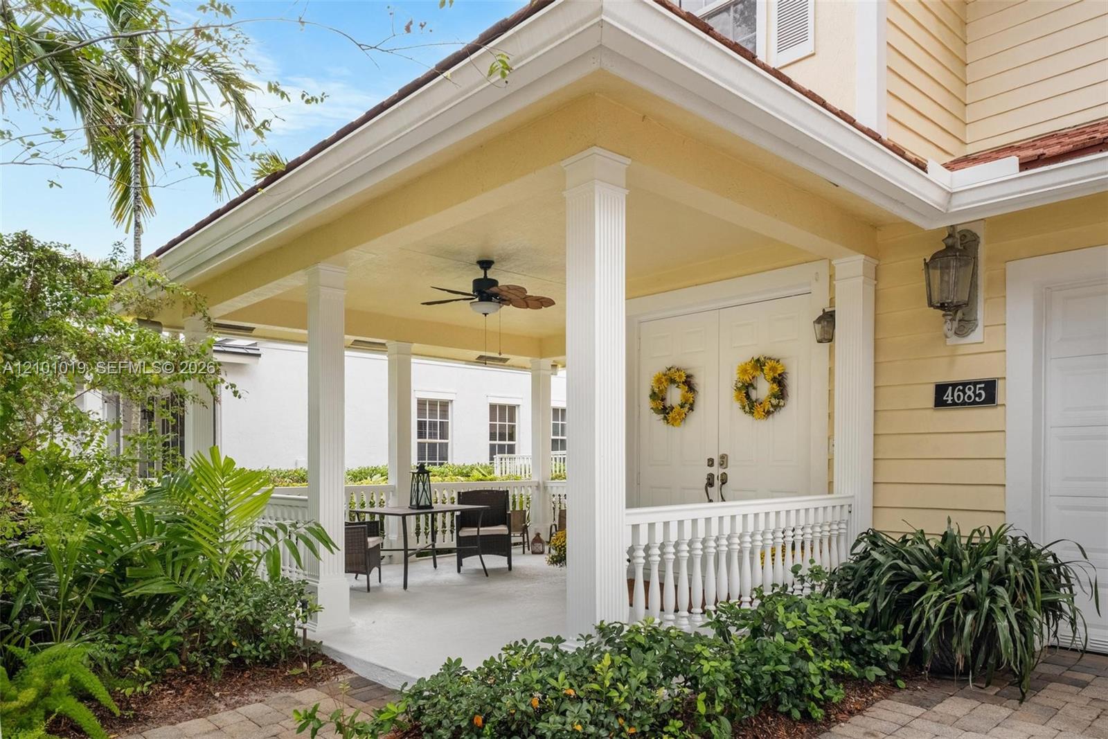 Covered entryway featuring a wrap-around porch with white balustrade railings, white columns, a ceiling-mounted fan, and double entry doors Covered entryway featuring a wrap-around porch with white balustrade railings, white columns, a ceiling-mounted fan, and double entry doors