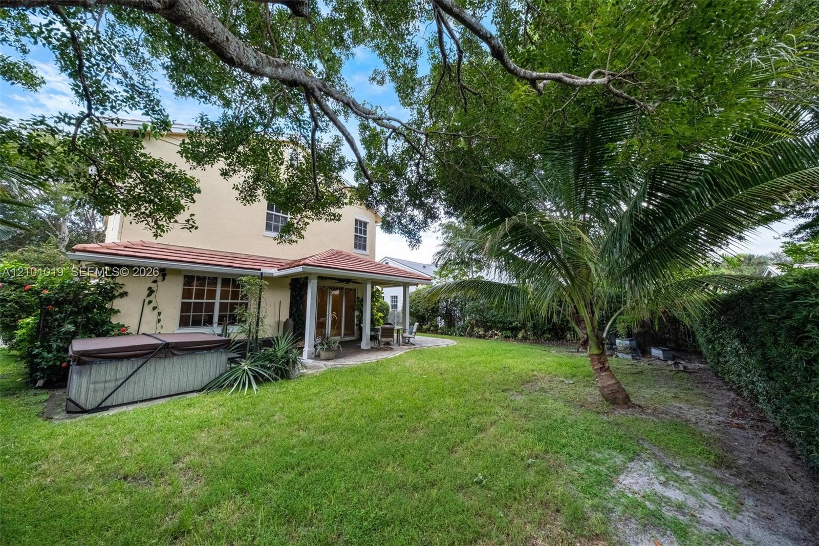 Rear exterior featuring a covered patio with tile roof, mature landscaping, and a manicured lawn