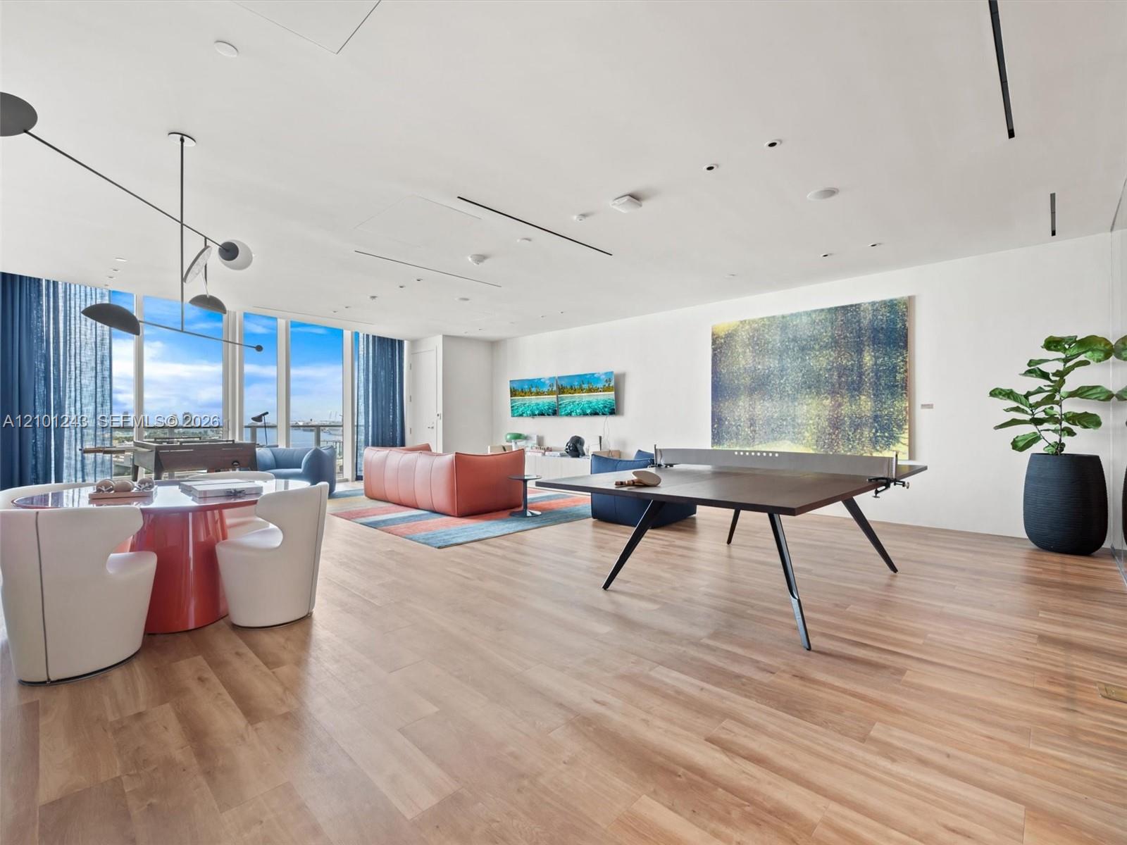 Open-concept interior featuring floor-to-ceiling windows, wood-finish flooring, recessed linear lighting, and modern multi-arm pendant lighting