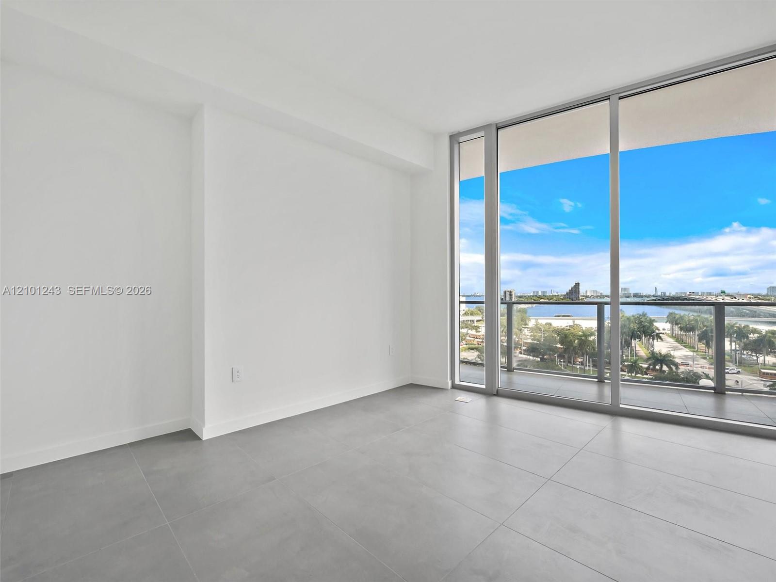 Floor-to-ceiling glass windows, ceramic tile flooring, and a covered balcony featuring a glass panel railing