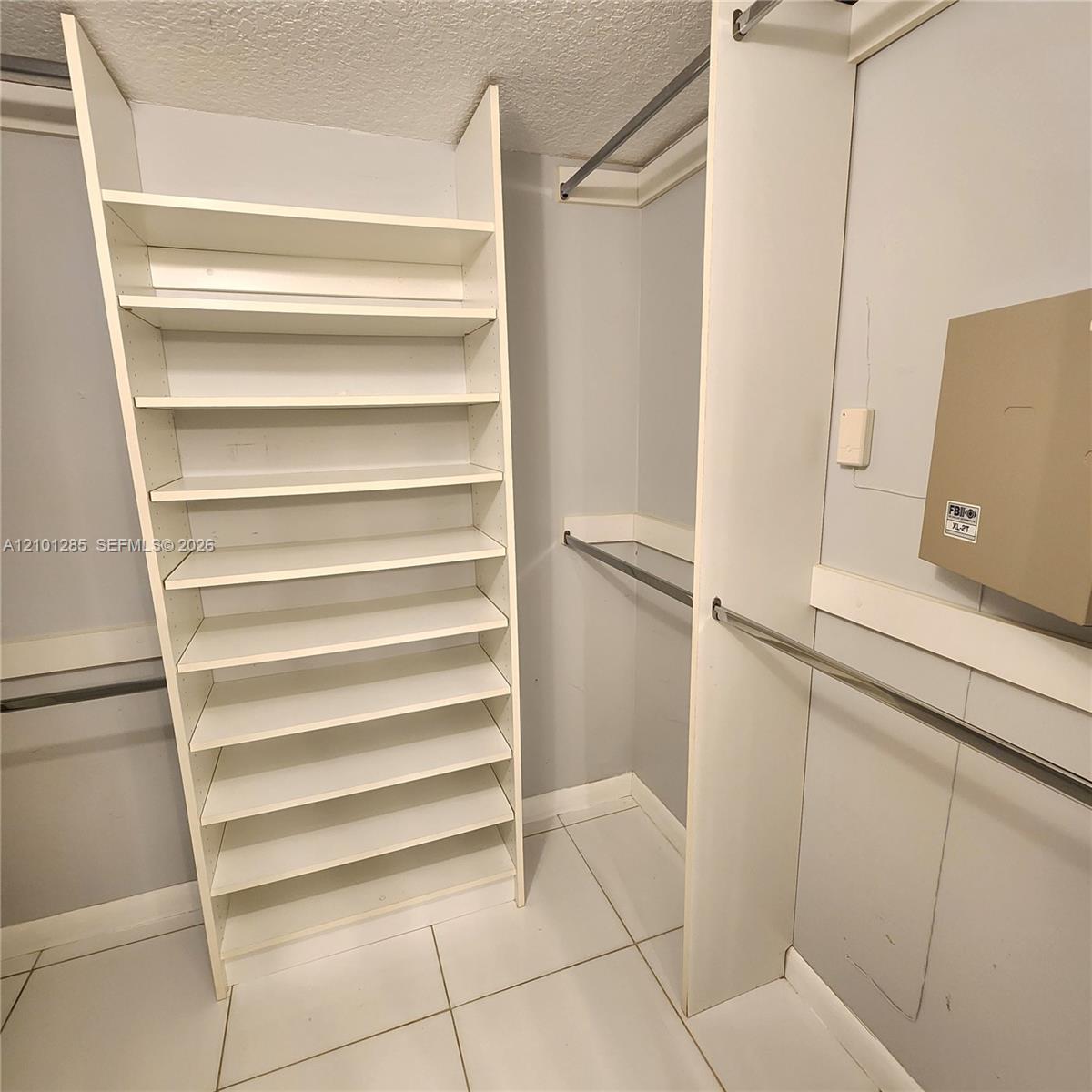 Custom walk-in storage featuring multi-level white shelving, horizontal metal hanging rods, and tile flooring