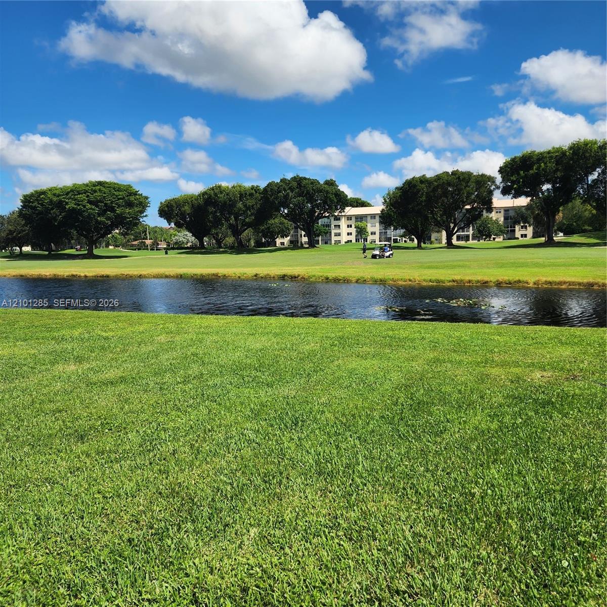 Expansive grounds featuring a manicured lawn, a central pond, and mature trees
