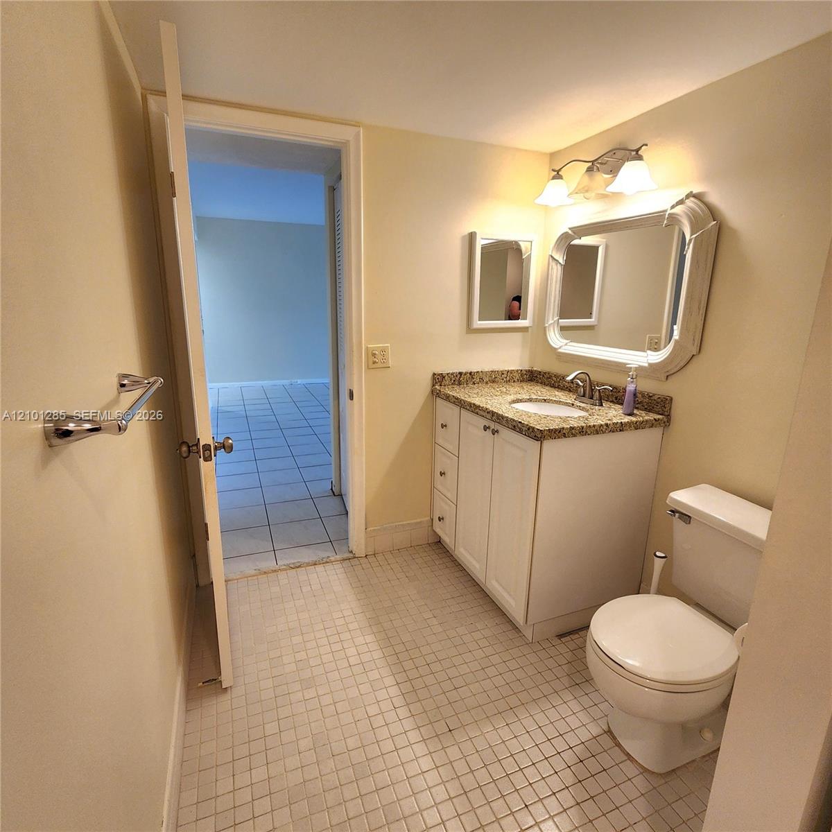 Bathroom featuring a vanity with stone-finish countertop, undermount sink, decorative wall mirror, and ceramic tile flooring