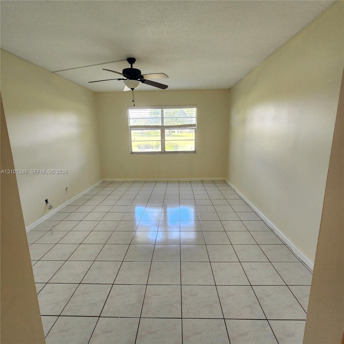 Room featuring neutral wall paint, white tile flooring, large horizontal window, and a ceiling fan with integrated lighting