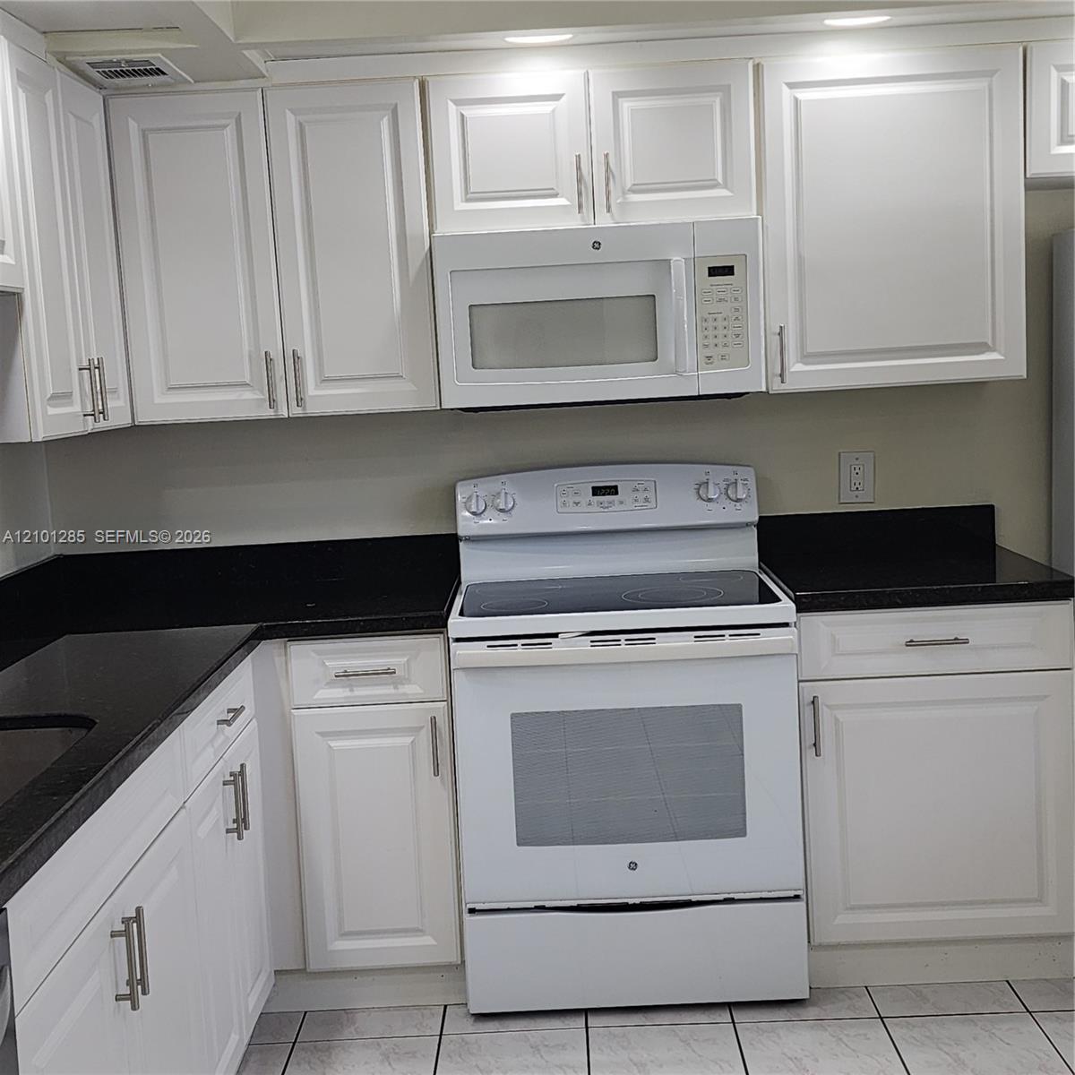 Kitchen featuring white shaker-style cabinetry, dark stone-finish countertops, and white appliances including an electric range and built-in microwave