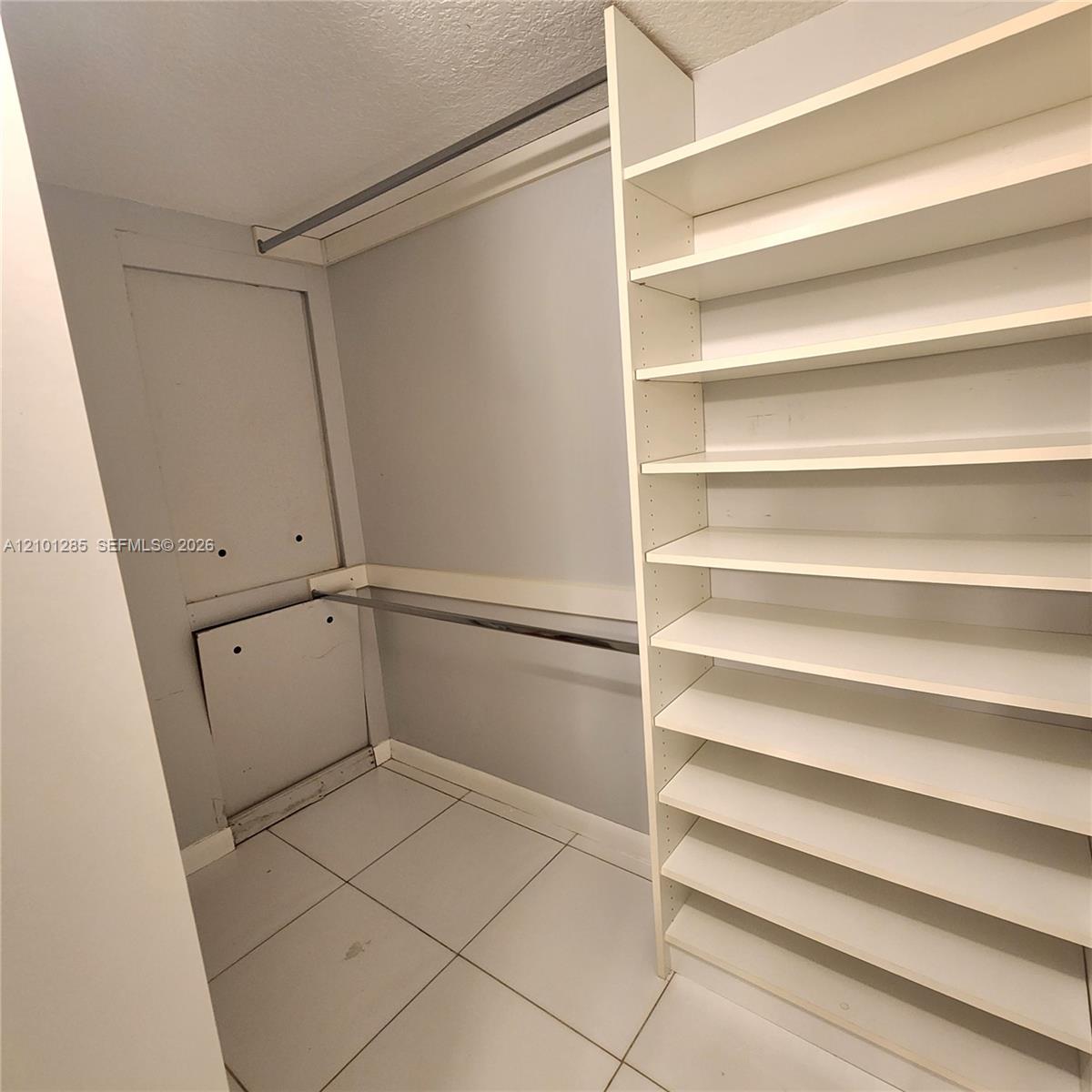 Walk-in storage space featuring ceramic tile flooring, built-in shelving, and dual metal clothing rods