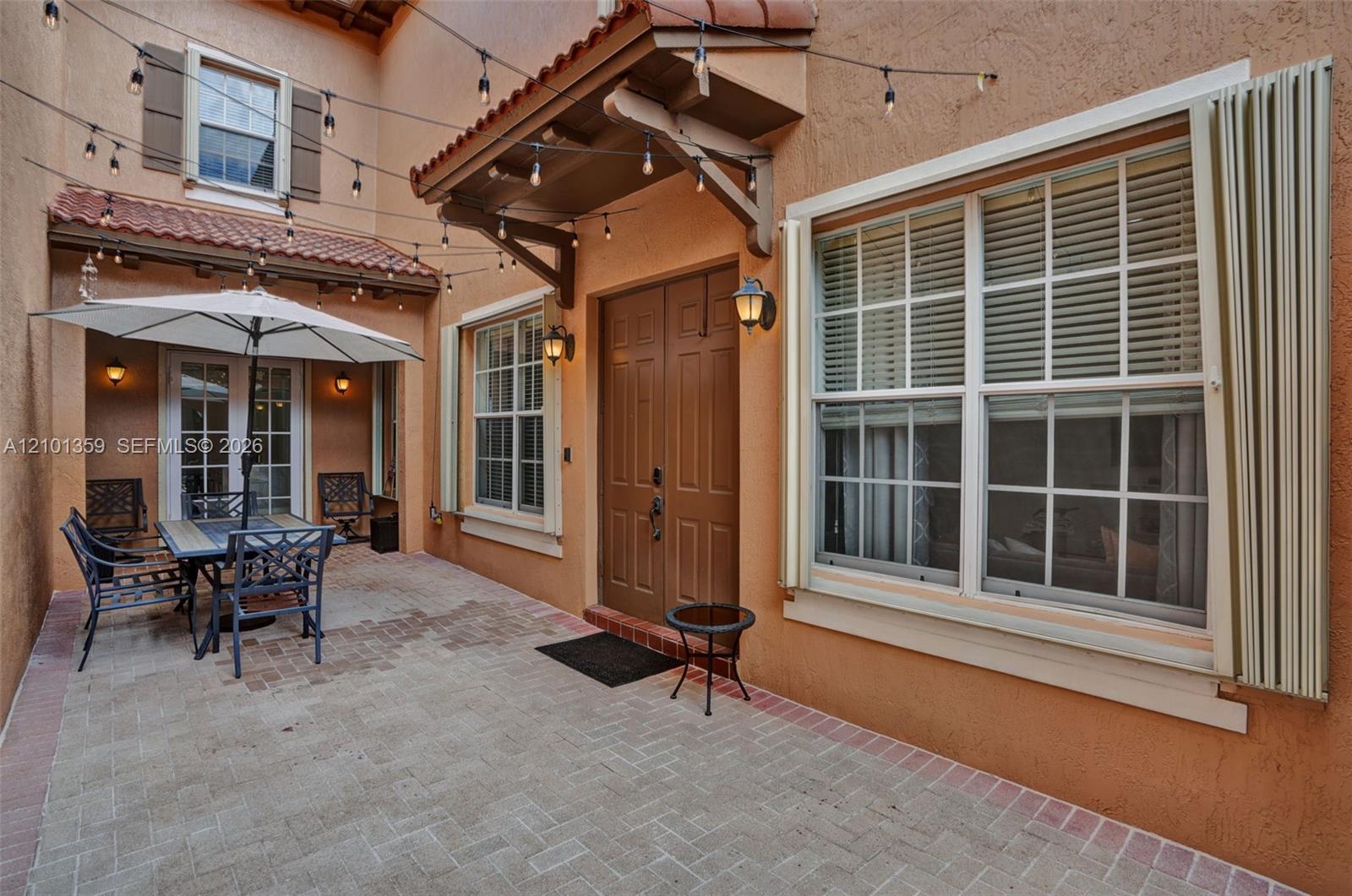 Enclosed courtyard featuring a paved brick patio, double entry doors, clay-tile roofing accents, and wall-mounted exterior lighting