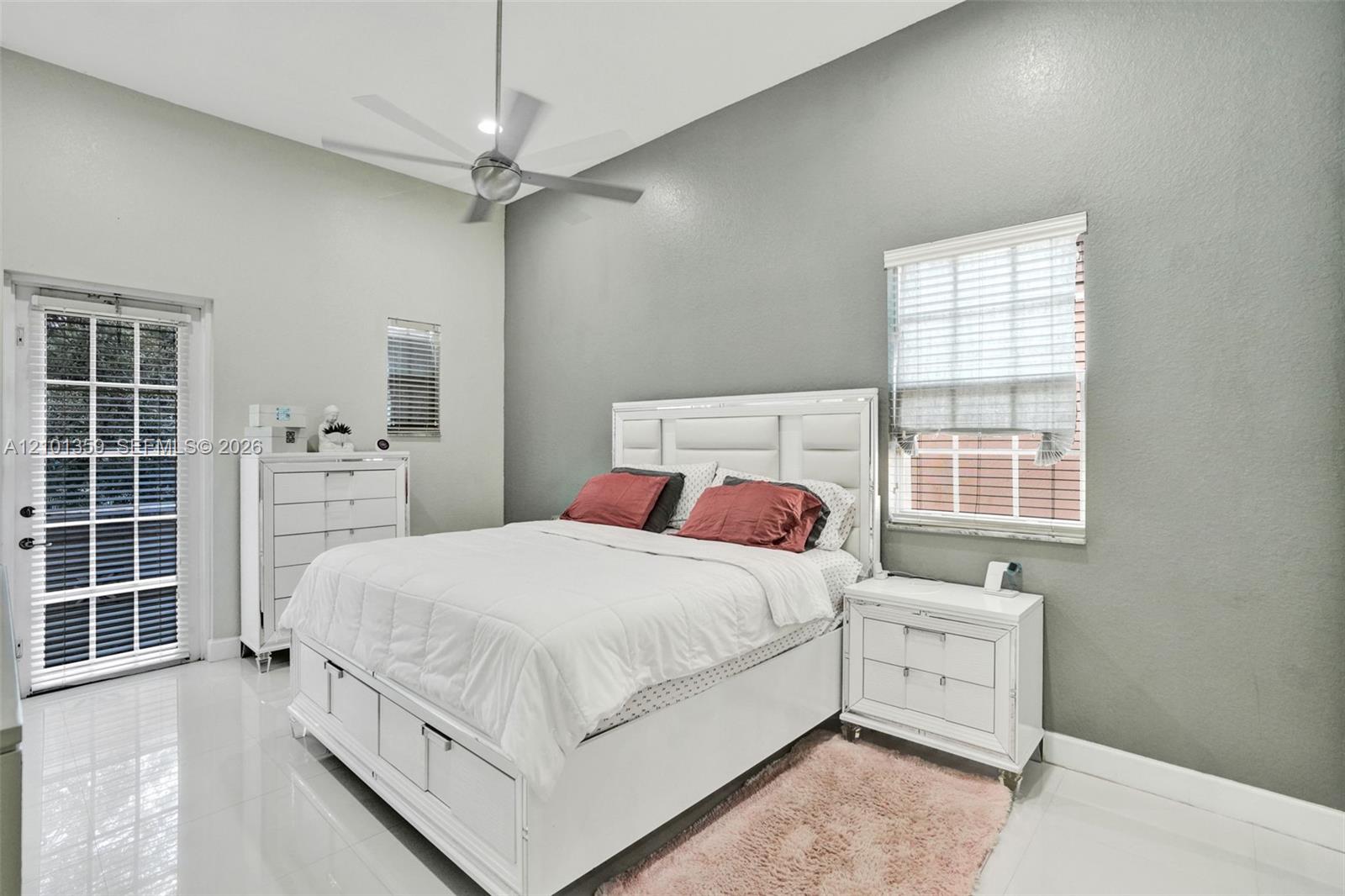 High-ceilinged bedroom featuring glossy tile flooring, a multi-blade ceiling fan, and a glass-paned exterior door