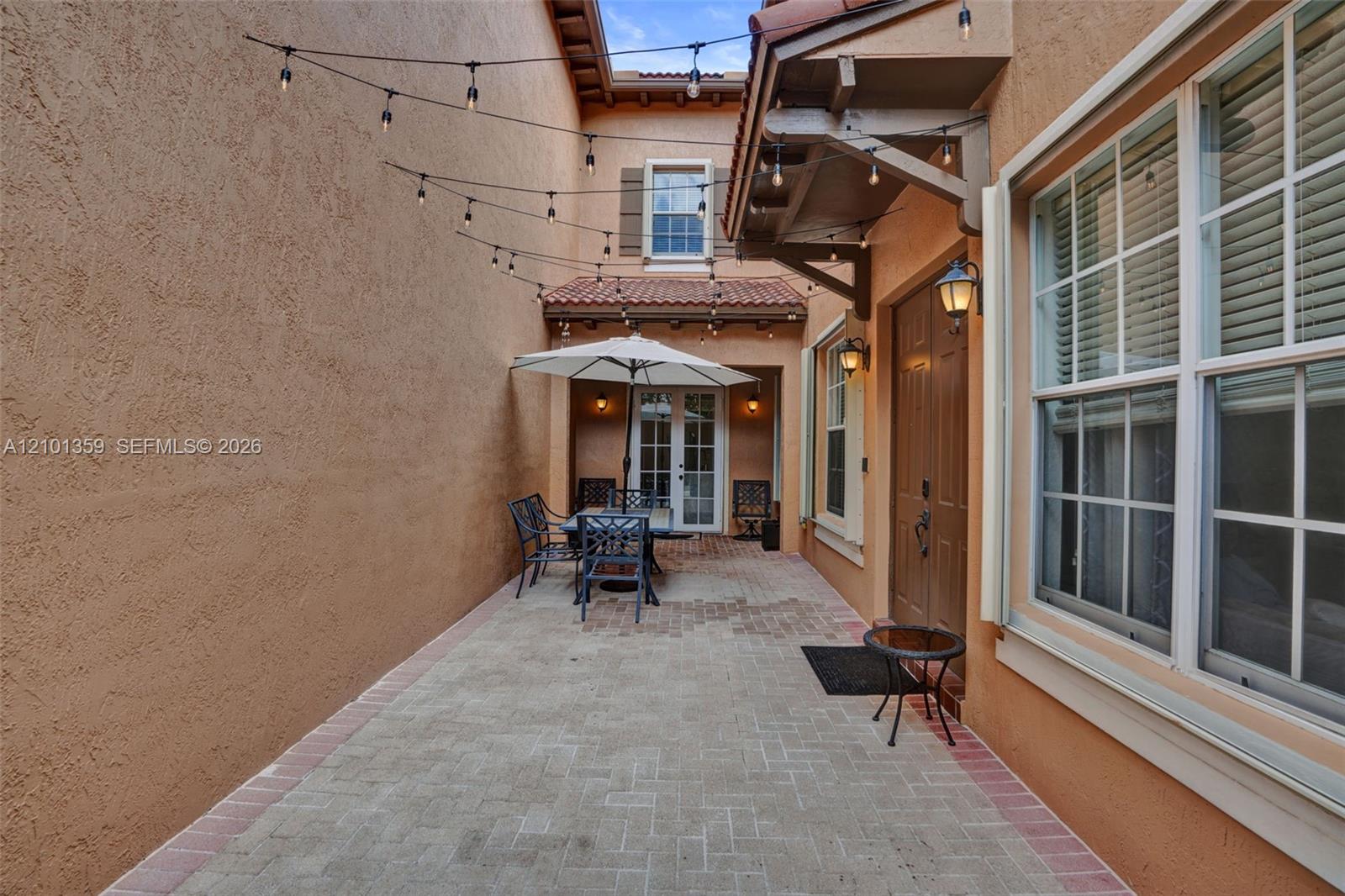 Enclosed courtyard featuring herringbone-patterned brick pavers, dual entry doors, multi-pane windows, and a clay tile roof