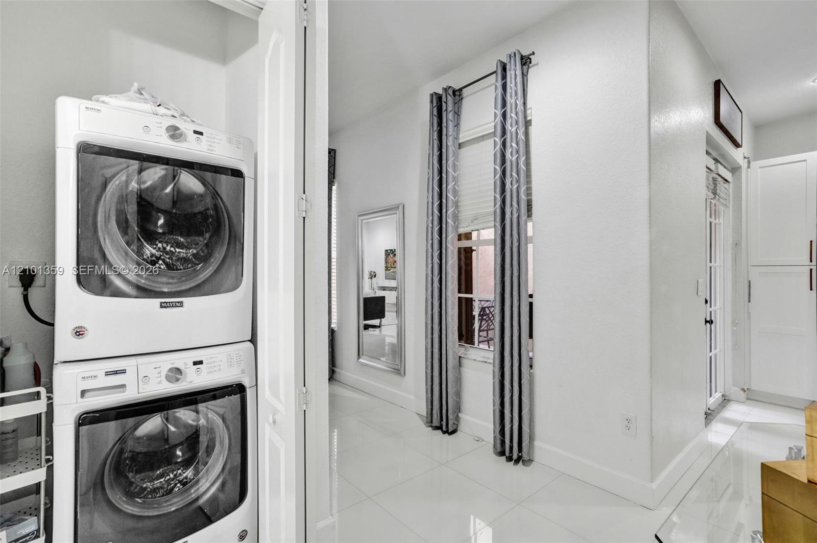 Laundry area featuring stacked front-load appliances, tile flooring, window with blind, and built-in cabinetry