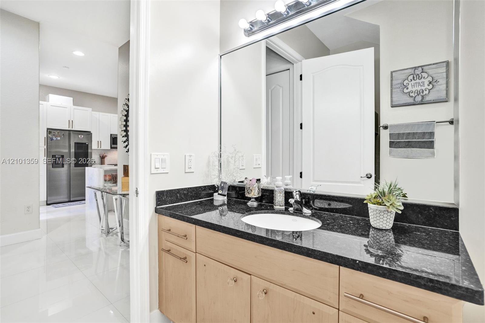 Bathroom vanity featuring dark stone countertops, an integrated undermount sink, light wood-finish cabinetry, a large wall-mounted mirror, and a multi-bulb light fixture