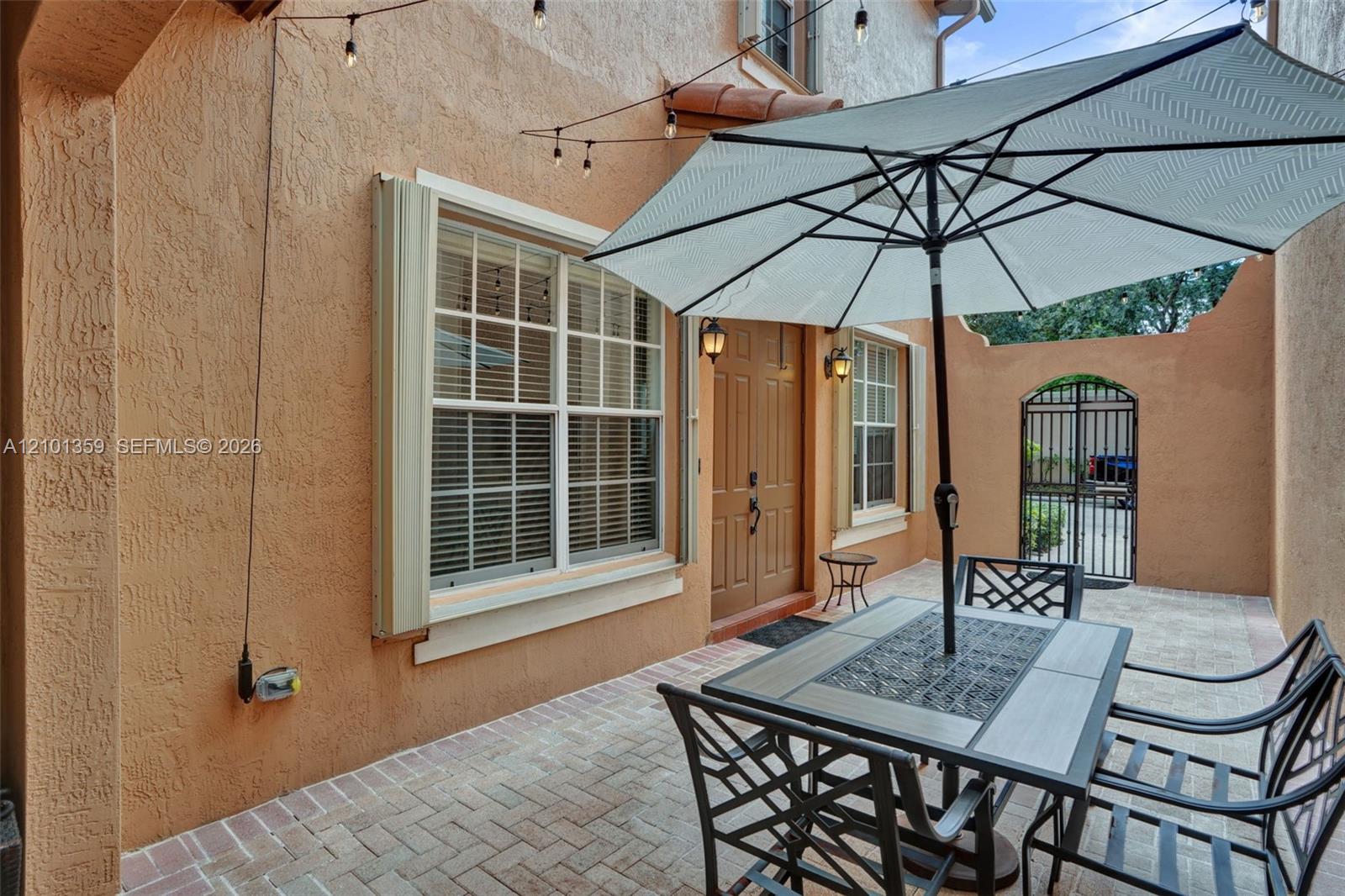Stucco exterior courtyard featuring herringbone-patterned paver flooring, double-entry doors, and a decorative wrought-iron gate