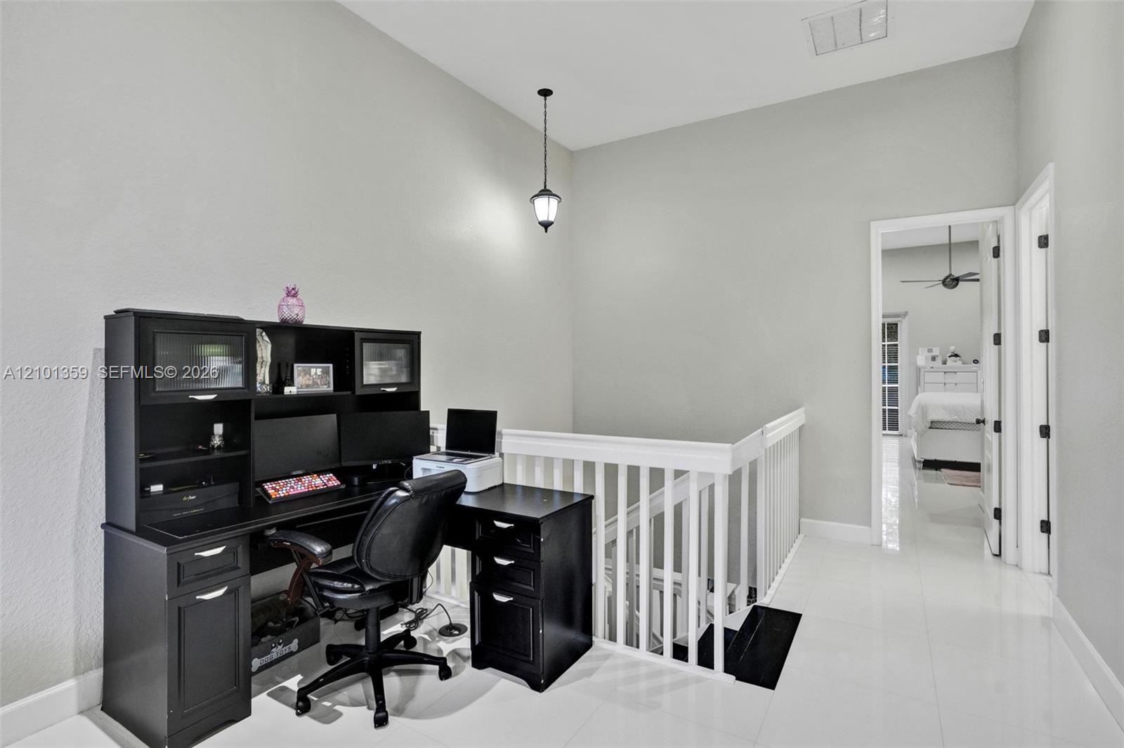 High-ceiling landing featuring glossy tile flooring, a white wooden balustrade, and a hanging pendant light