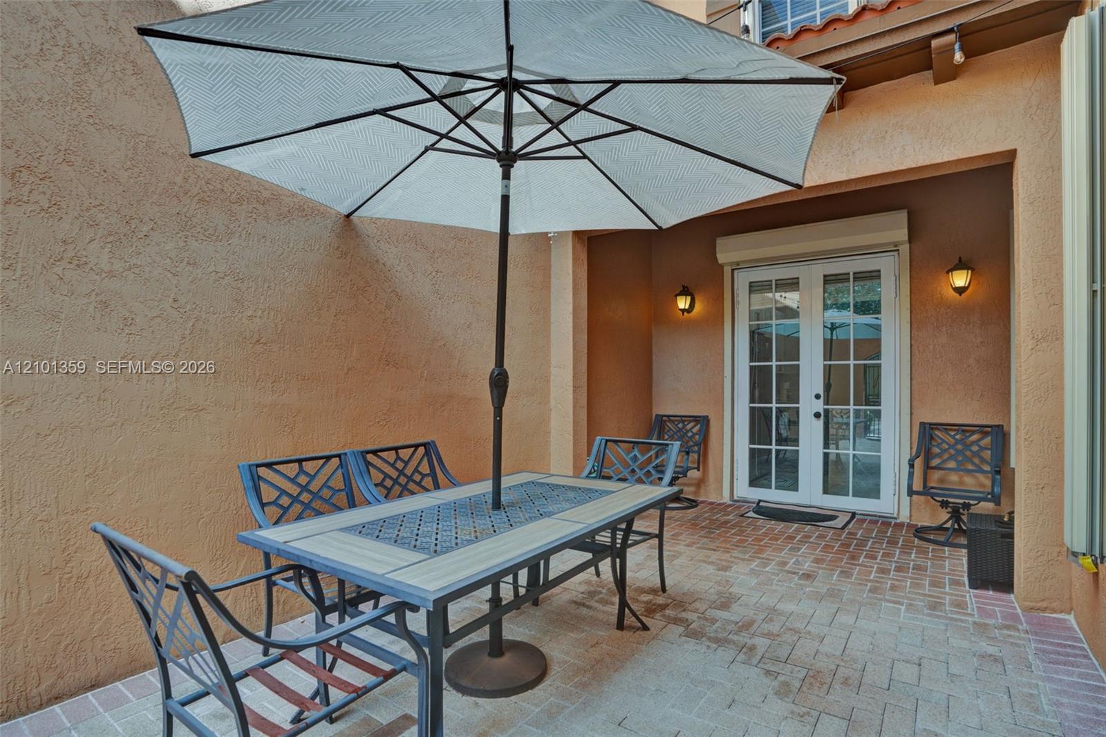 Enclosed patio featuring stucco walls, paver flooring, French doors, and wall-mounted exterior lighting