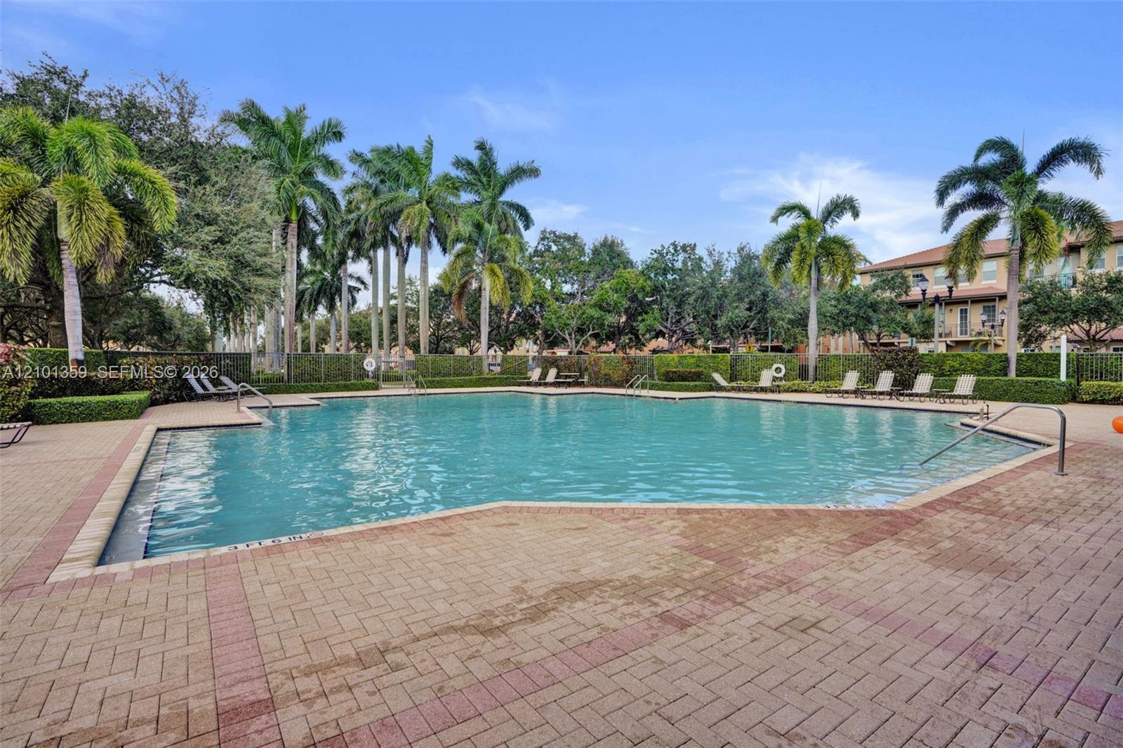 Swimming pool with stone-paver decking, perimeter landscaping, and mature palm trees