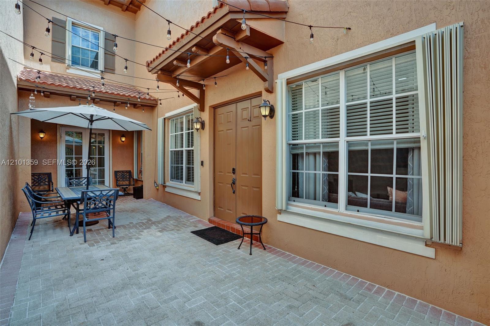 Enclosed courtyard featuring a paved brick patio, double entry doors, wood-accented awning, and exterior wall-mounted light fixtures