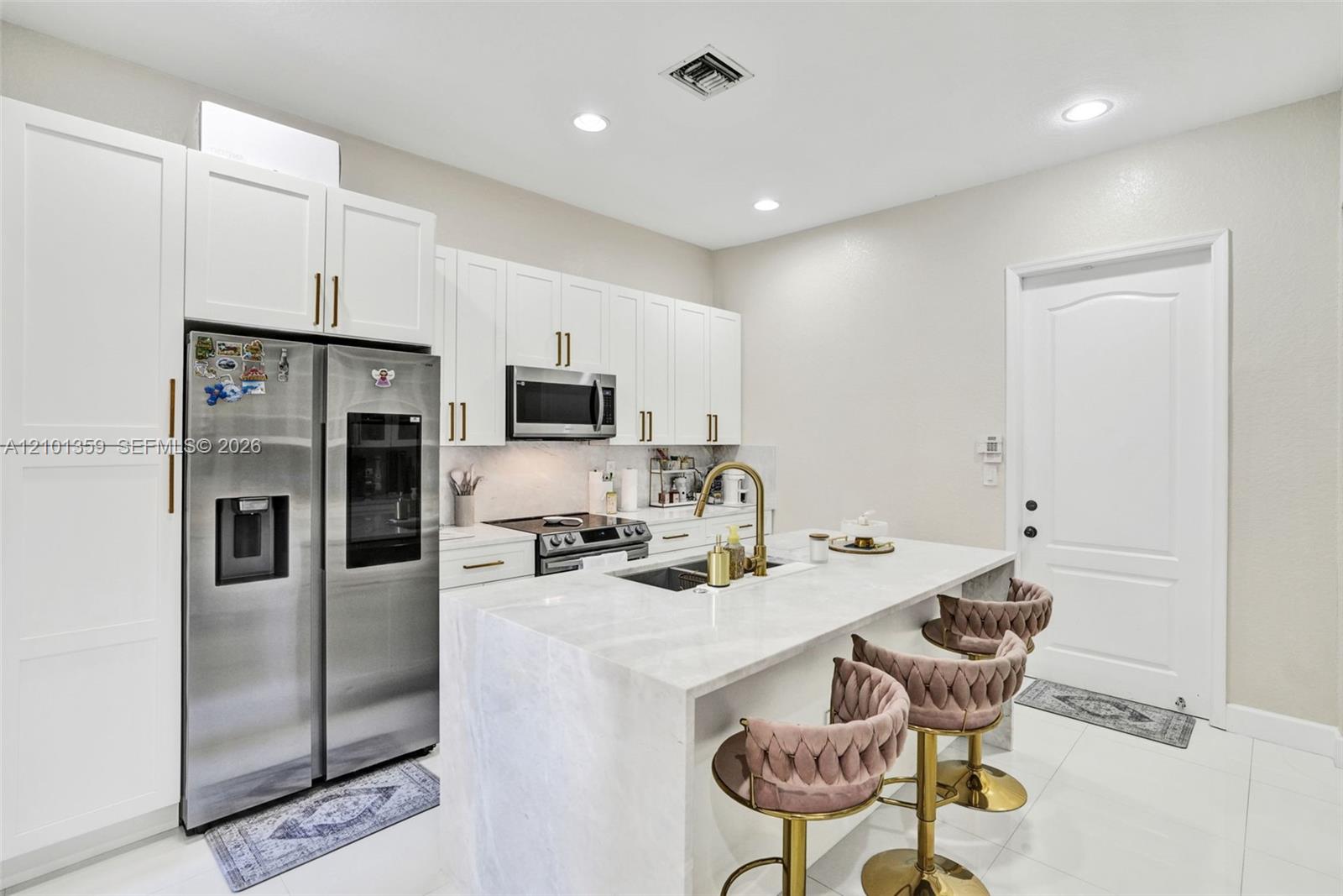Kitchen featuring white shaker-style cabinetry, a stone-surfaced waterfall island, stainless steel appliances, brass-toned hardware, and recessed lighting