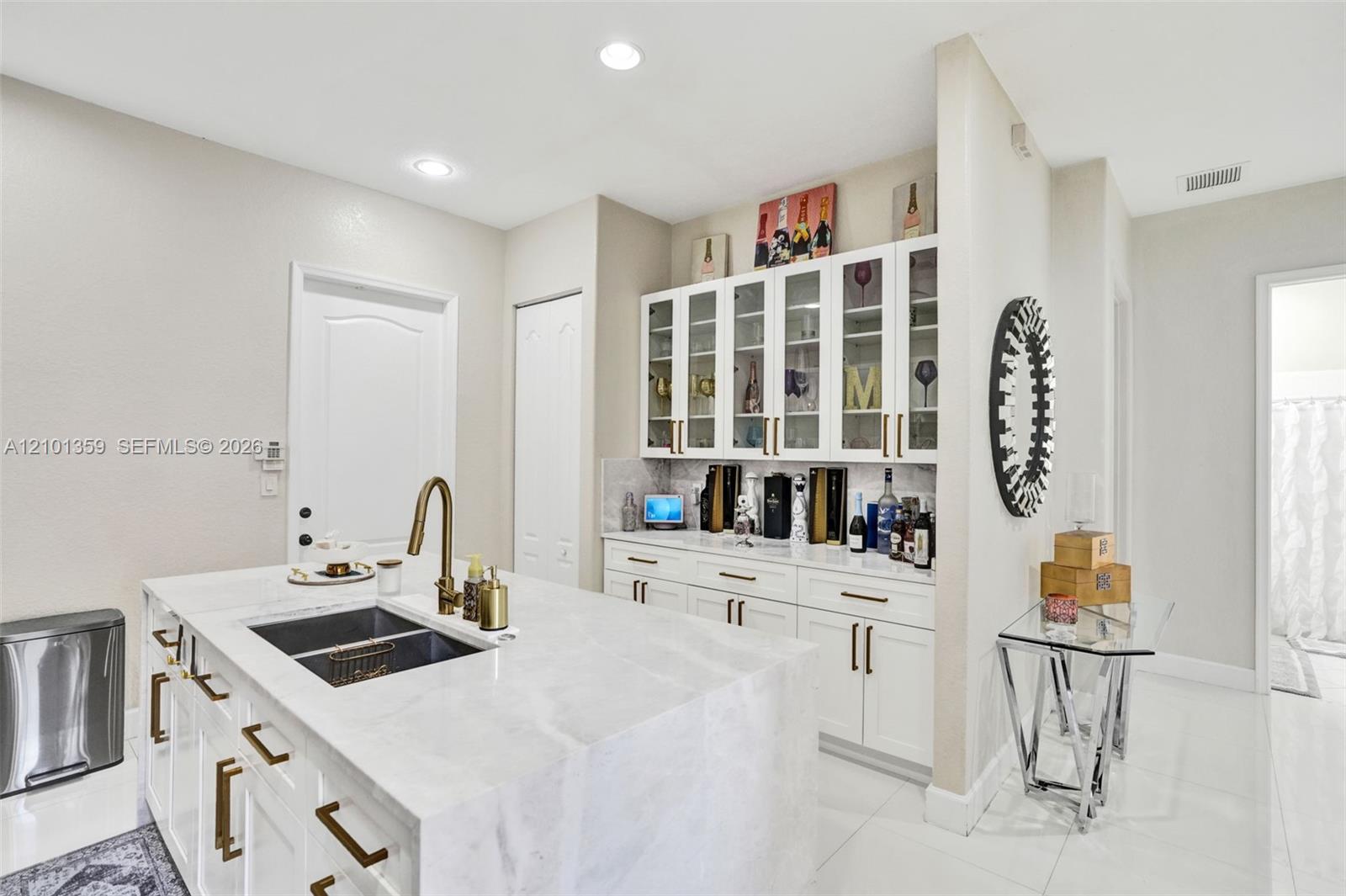 Kitchen island featuring stone countertops and an integrated dual-basin undermount sink with a high-arch faucet, paired with white built-in cabinetry and glass-front upper displays