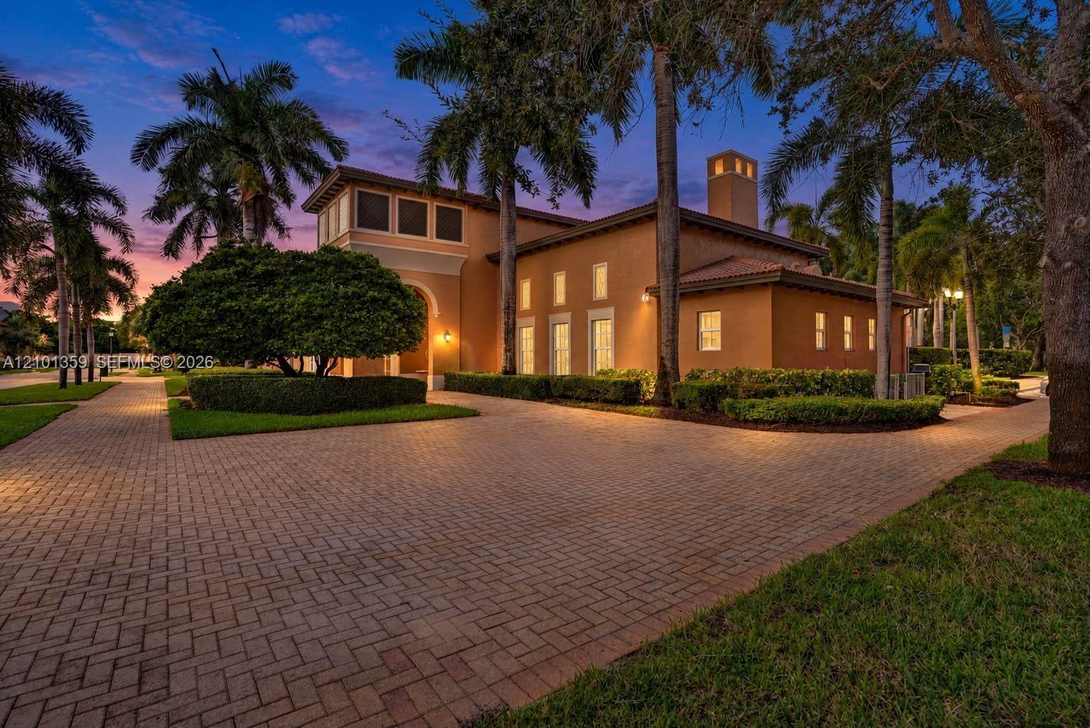 Stucco exterior featuring a paver driveway, multiple vertical windows, a prominent chimney, and mature palm trees