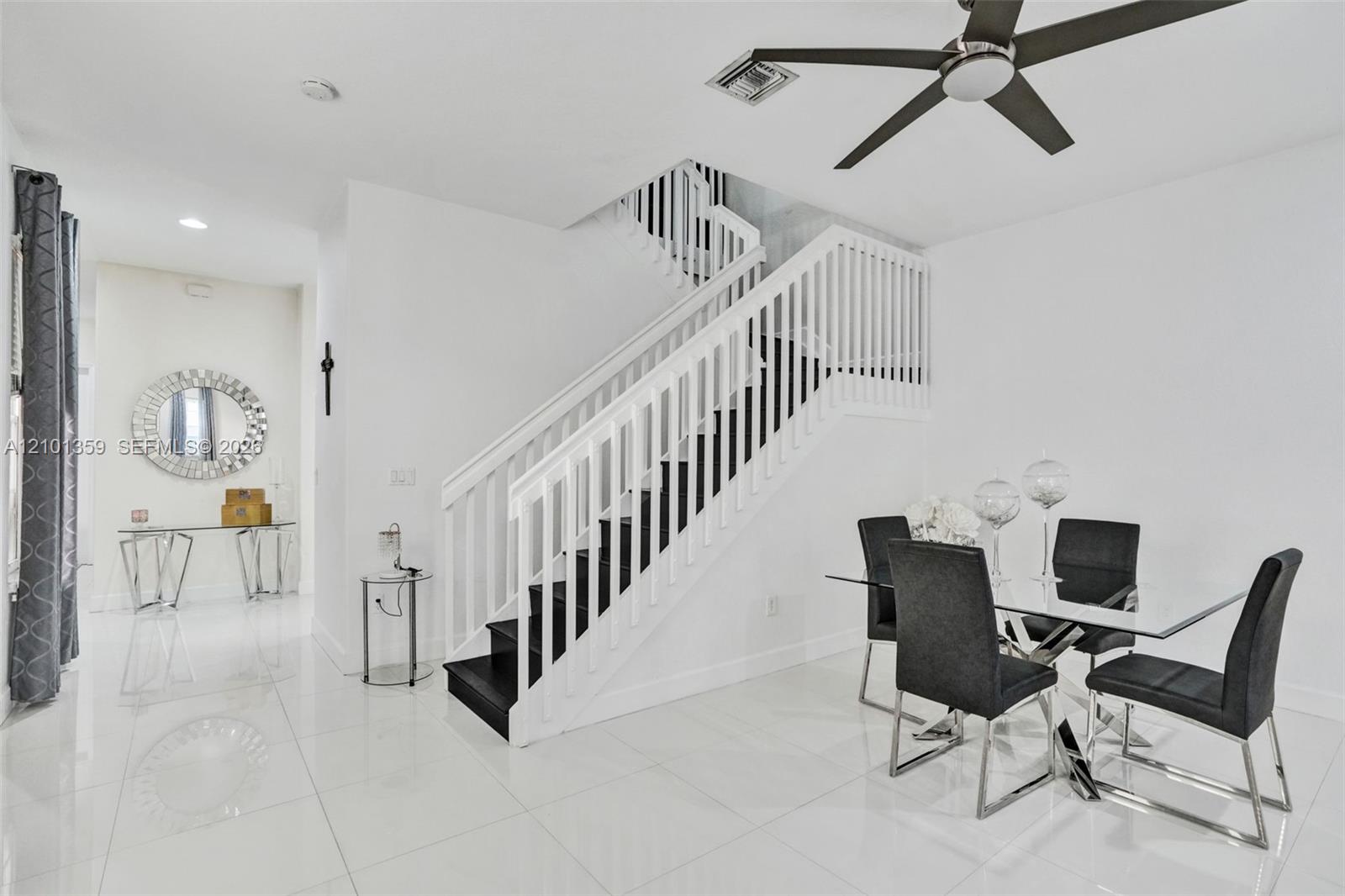 Staircase featuring white balusters and a contrasting dark-toned tread design, polished tile flooring, and a modern ceiling fan