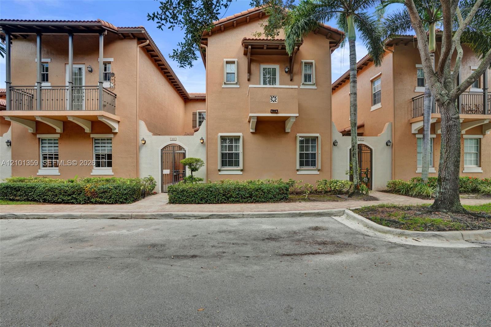 Mediterranean-style multi-level exterior featuring a stucco facade, decorative corbels, wrought-iron balcony railings, and arched courtyard gates